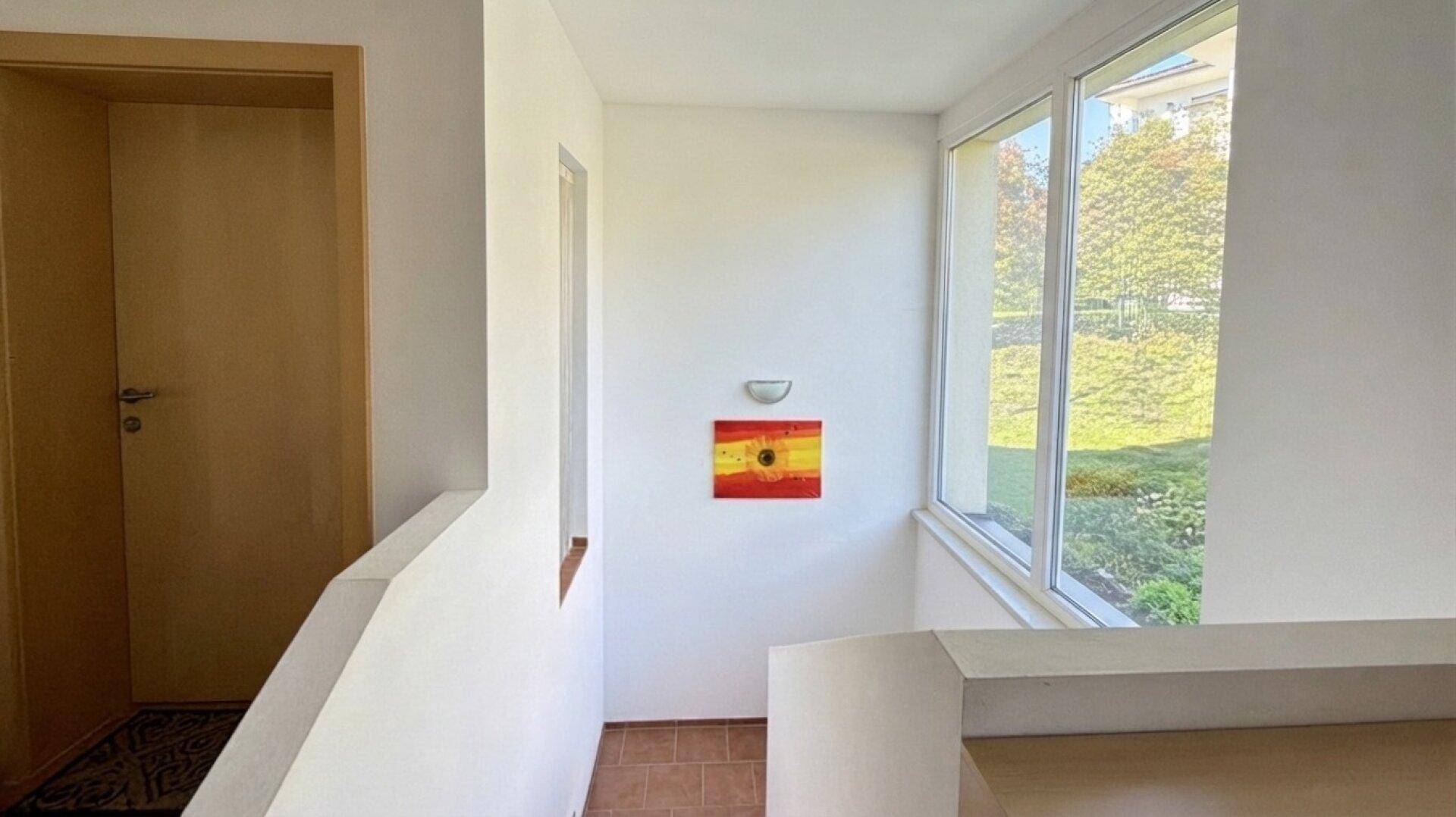Heller Treppenaufgang mit großen Fenstern und Blick ins Grüne.