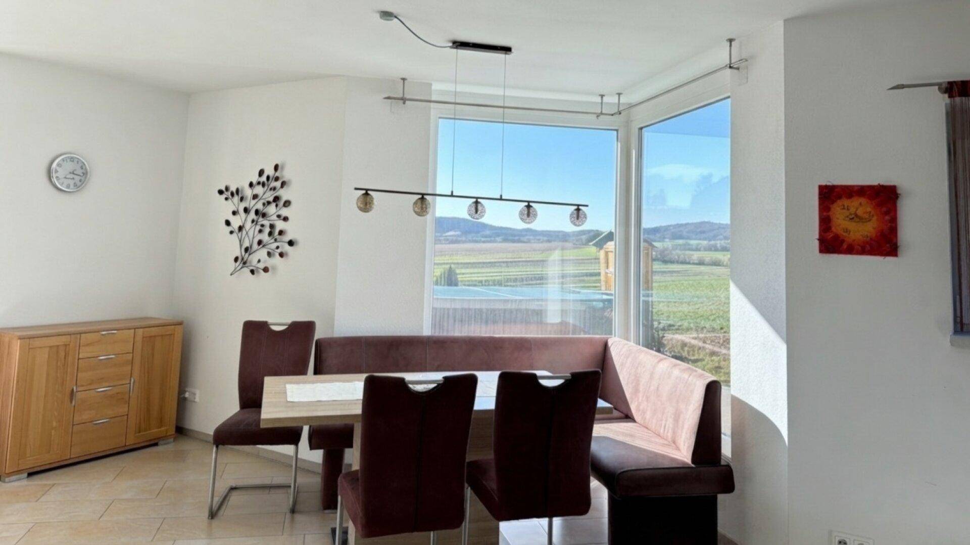 Heller Essbereich mit Eckbank, großem Fenster und Blick auf die Landschaft.