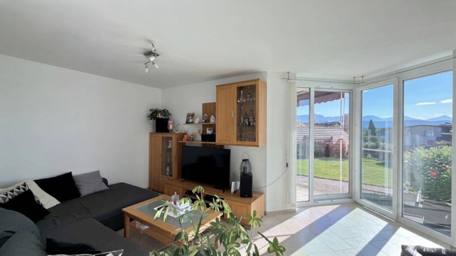 Helles Wohnzimmer mit Sofa, TV-Möbeln und großen Fenstern mit Bergblick.
