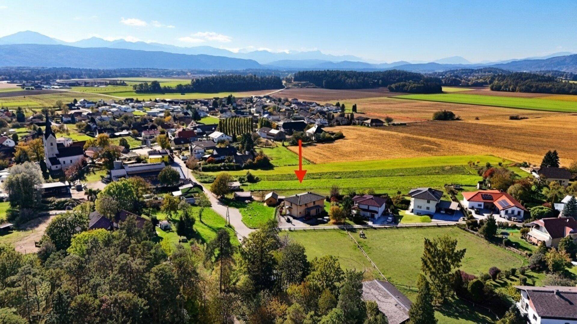 Weitläufige Luftaufnahme des Dorfes mit dem markierten Haus und der umliegenden Landschaft.