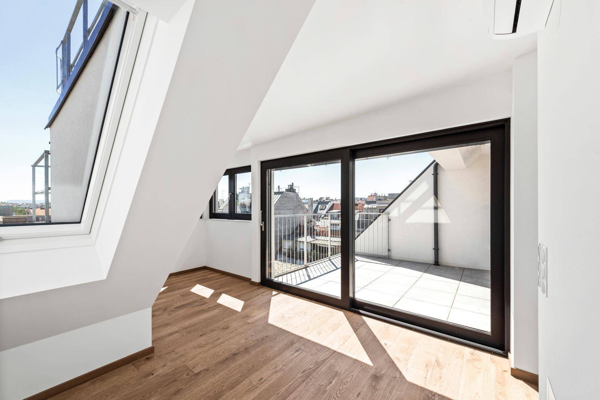 Lichtdurchfluteter Raum mit Holzboden und großer Schiebetür, die auf eine Dachterrasse führt.