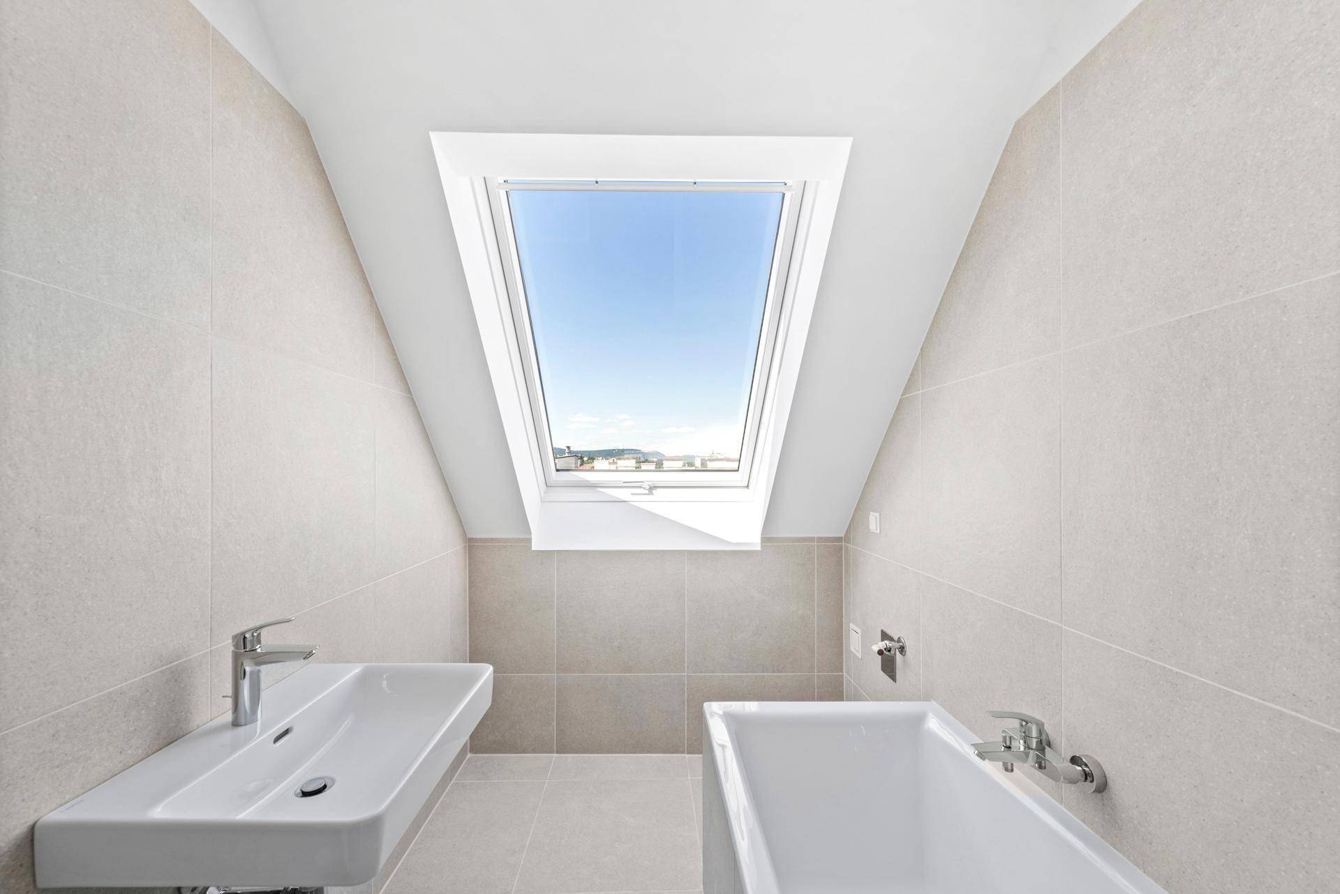 Modernes Badezimmer mit hellen Fliesen, Badewanne, Waschbecken und einem großen Dachfenster.