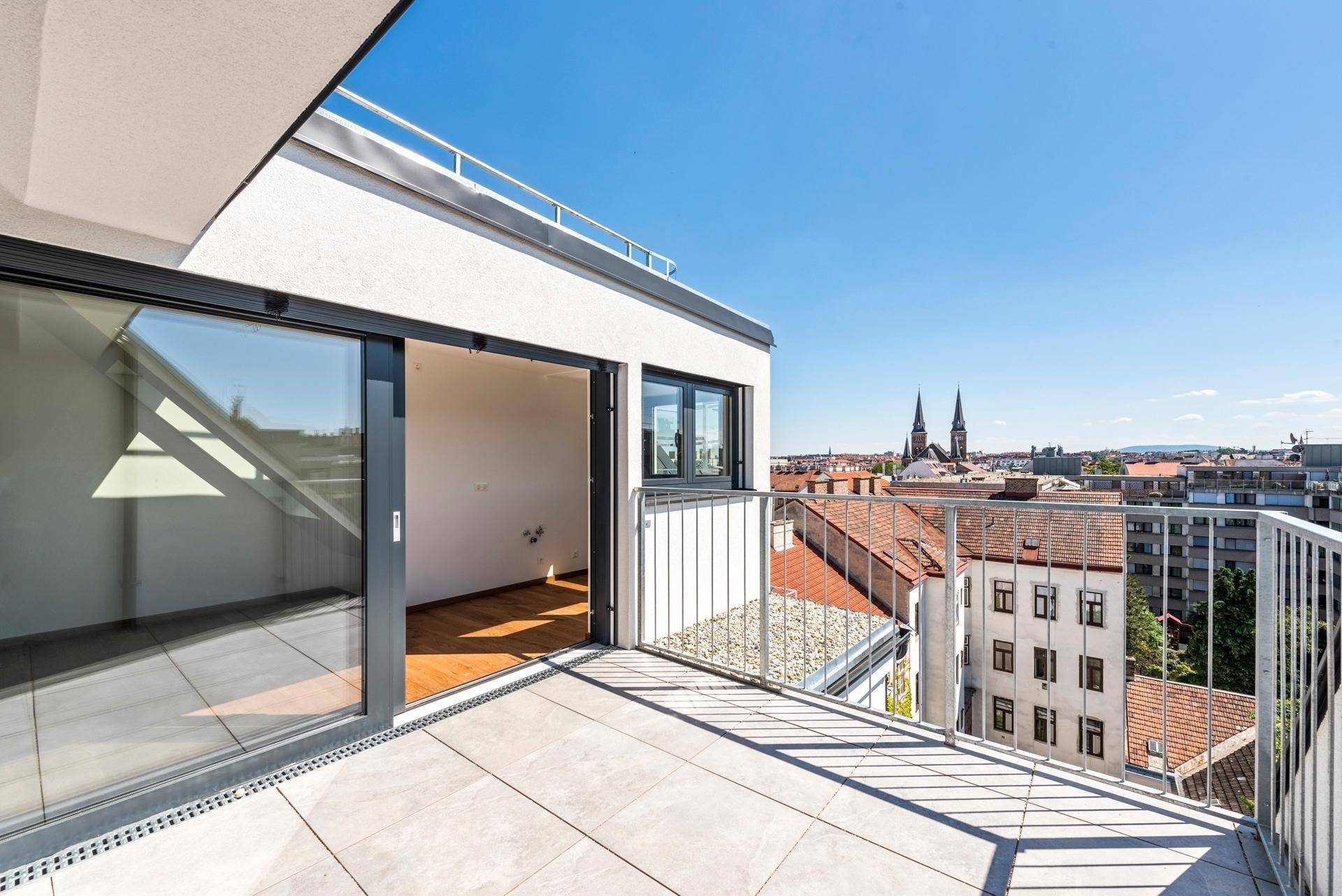 Geräumiger Balkon mit Fliesenboden und weitem Blick über die Stadt und Kirchtürme.