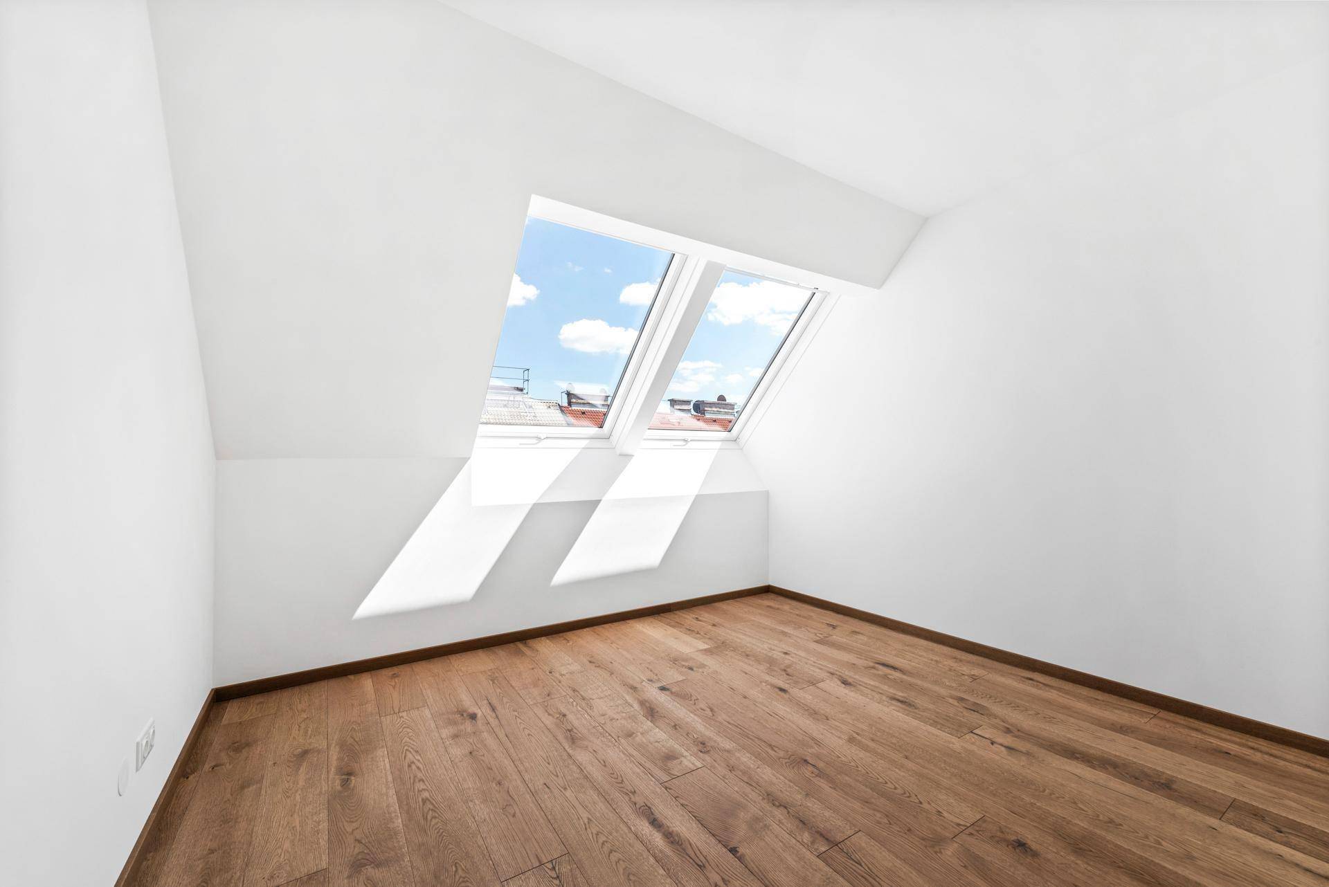 Heller Raum im Dachgeschoss mit Holzboden und zwei schrägen Dachfenstern, die viel Licht hereinlassen.