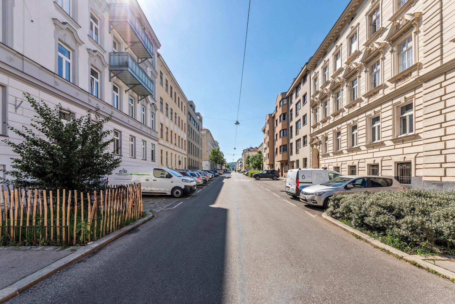 Ruhige Wohnstraße mit geparkten Autos und Bäumen, umgeben von klassischen Stadtgebäuden.