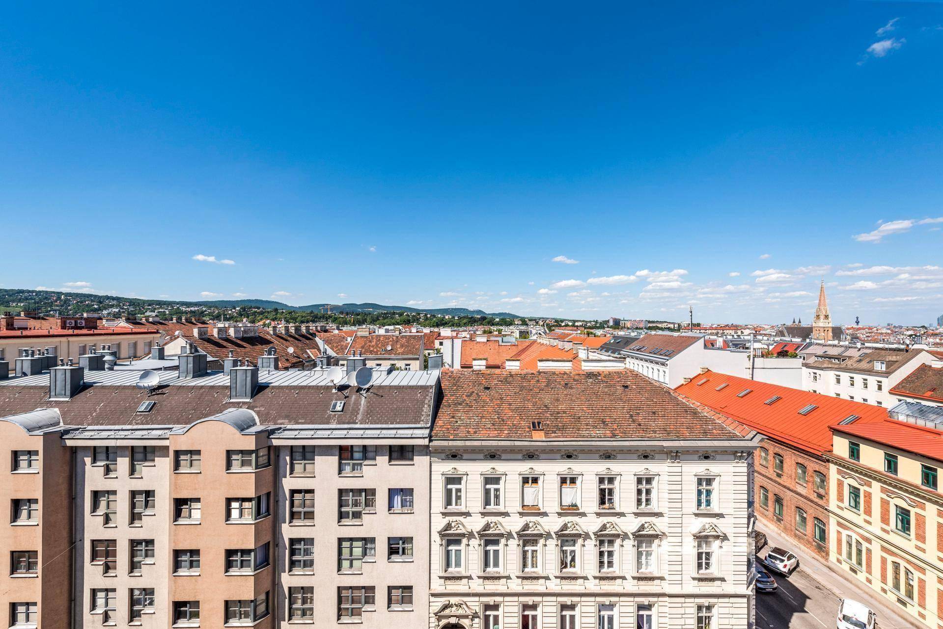 Panoramablick über die Dächer der Stadt mit Bergen im Hintergrund unter blauem Himmel.