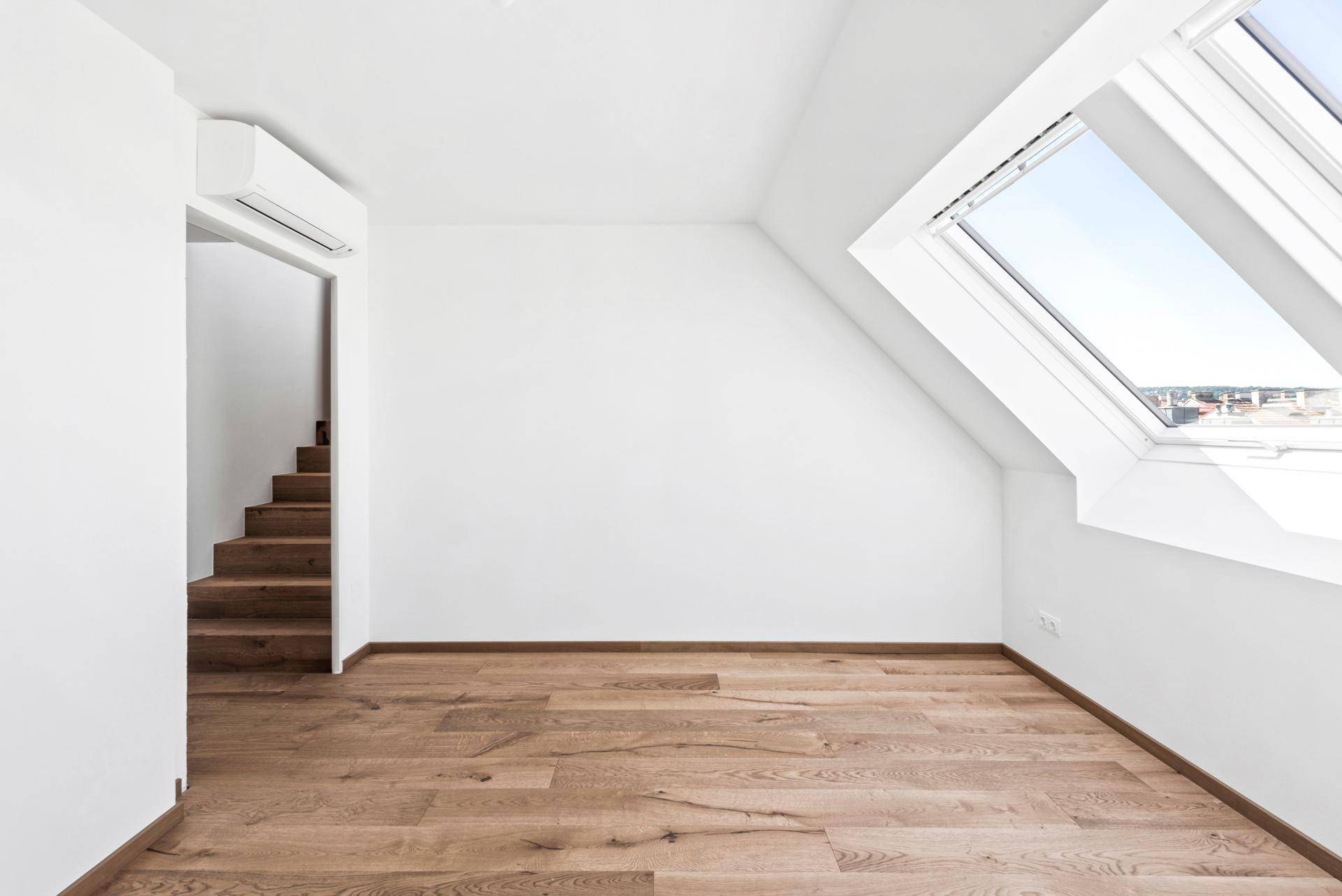 Helles Dachgeschosszimmer mit Holzboden, Dachfenster, Klimaanlage und Zugang zu einer Treppe.