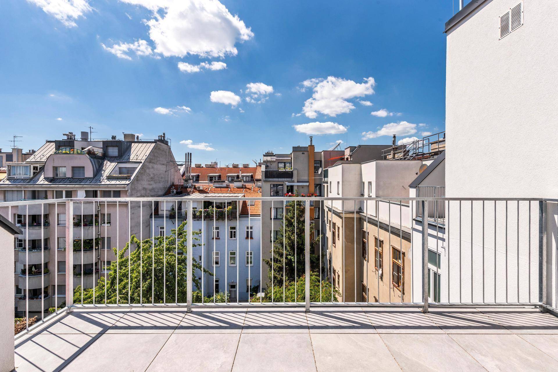 Sonniger Balkon mit Fliesenboden und Blick auf die umliegenden Gebäude und Dächer der Stadt.