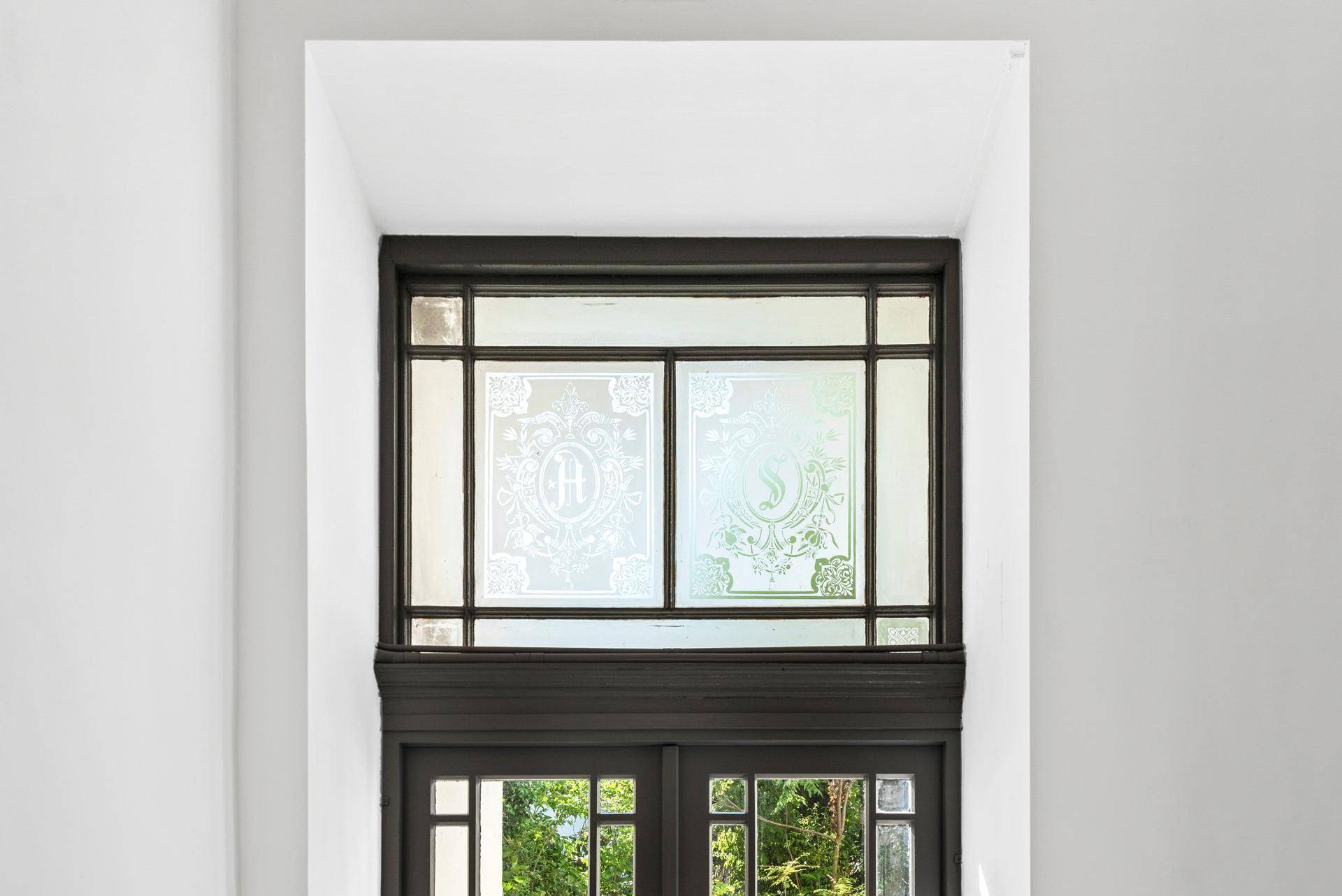 Detailansicht eines Fensters mit dekorativer Verglasung und Blick ins Grüne.