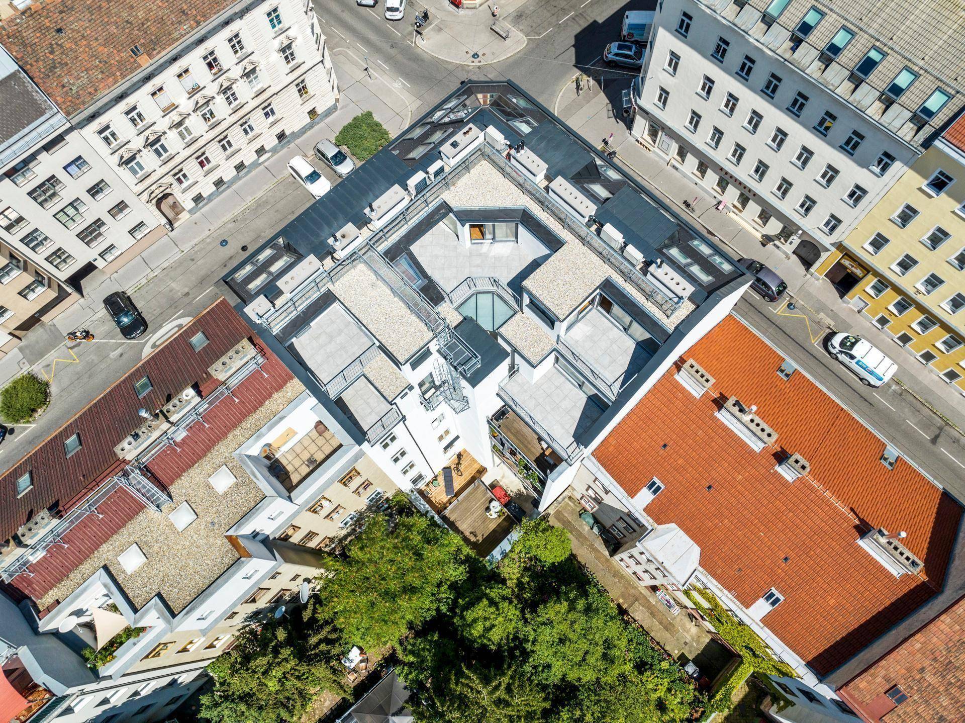 Luftaufnahme eines modernen Gebäudekomplexes mit Dachterrassen und Innenhof in städtischer Umgebung.