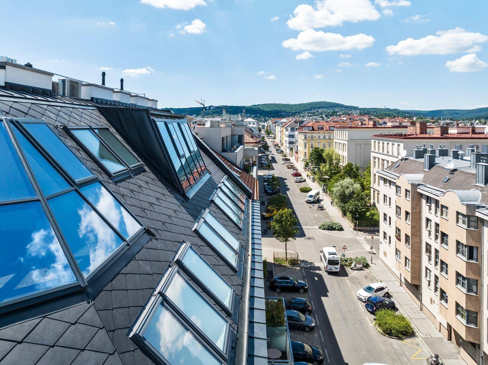 Weitblick über die Stadt mit einer belebten Straße und grünen Hügeln im Hintergrund unter blauem Himmel.