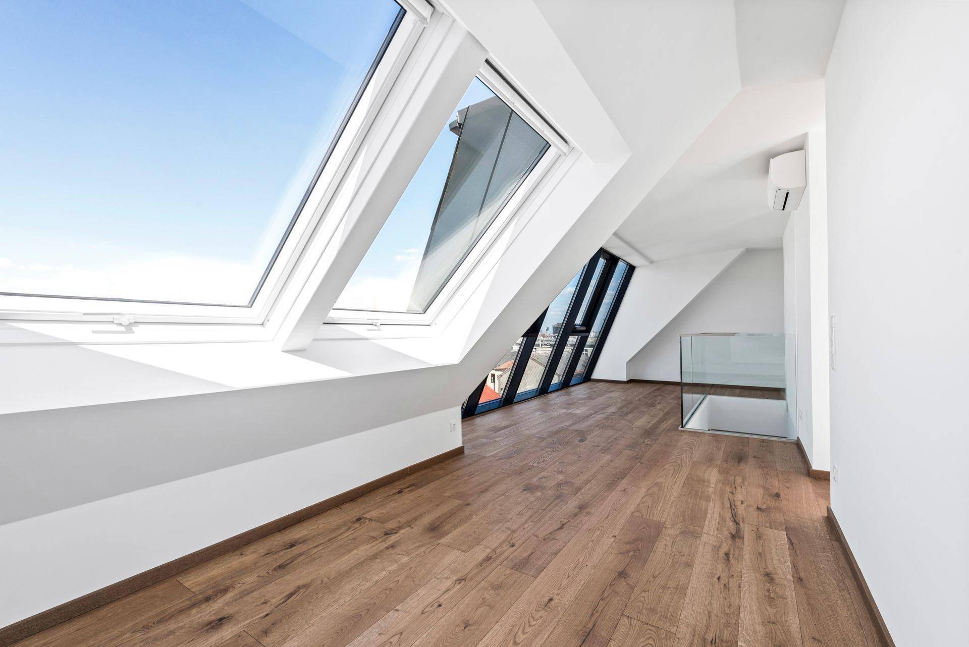 Geräumiger Dachgeschossraum mit Holzboden, mehreren Dachfenstern und einer modernen Glasbrüstung.