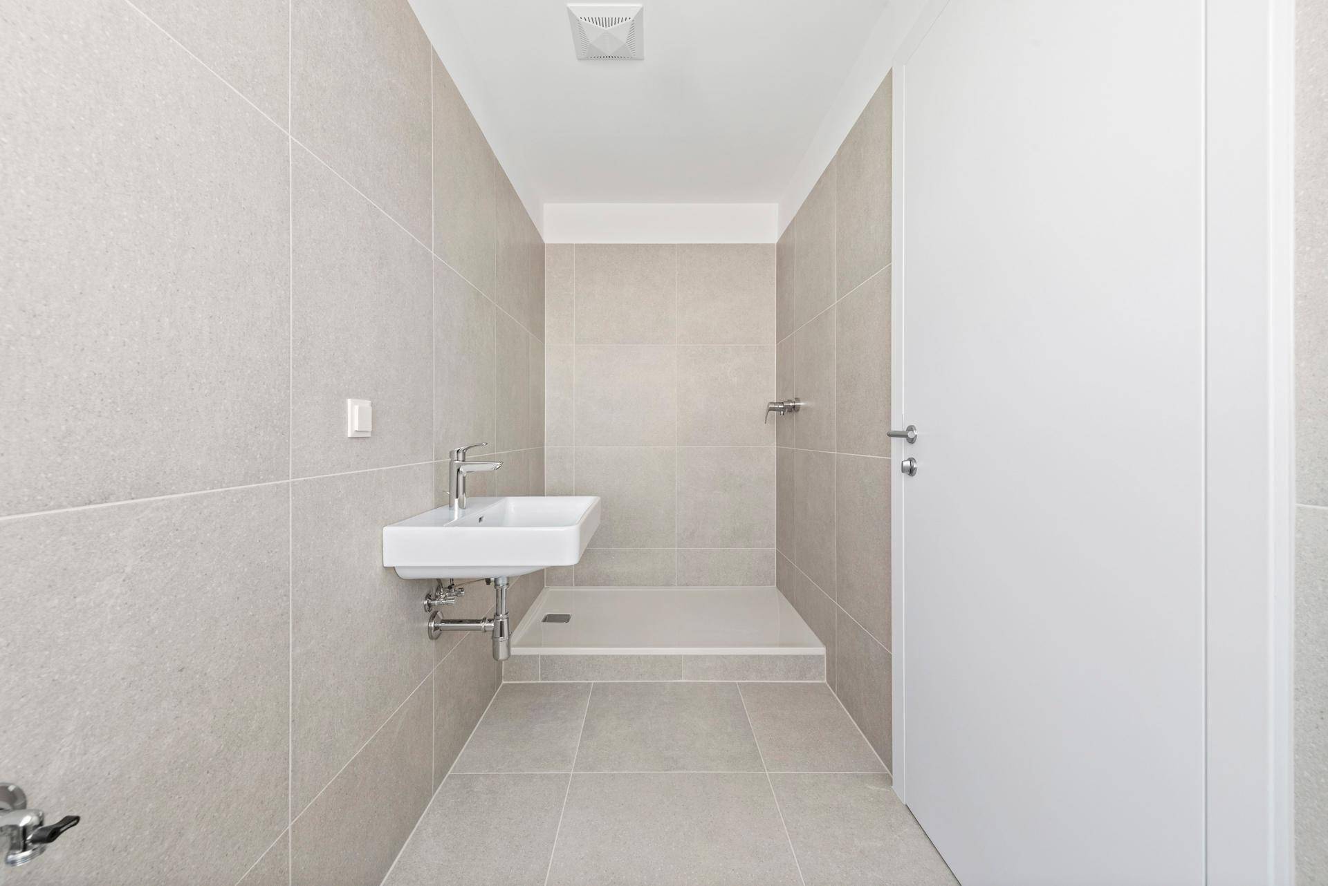 Modernes Badezimmer mit hellen Fliesen, ebenerdiger Dusche und einem einzelnen Waschbecken.