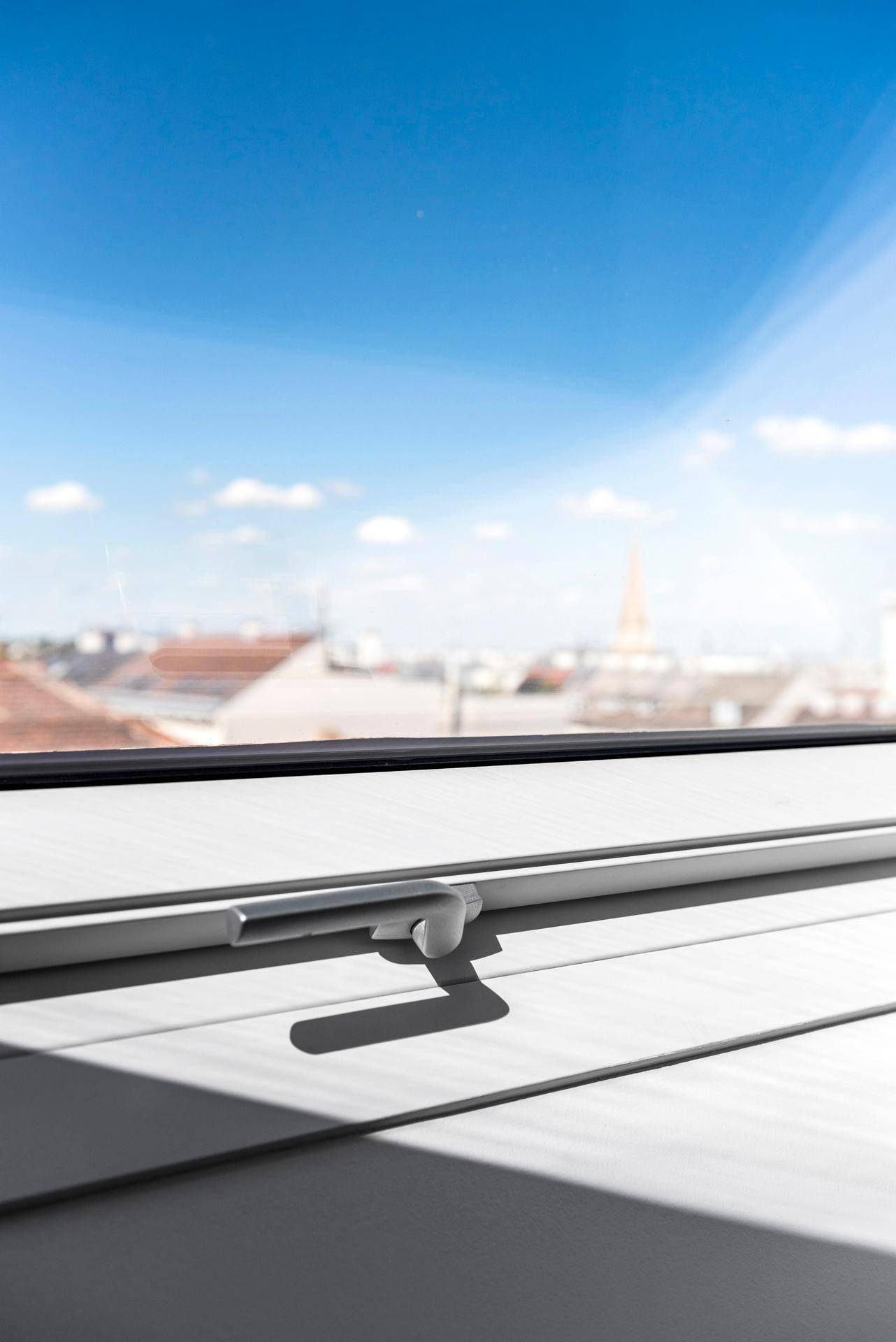 Nahaufnahme eines Dachfensters mit Blick auf die Stadt und den blauen Himmel.
