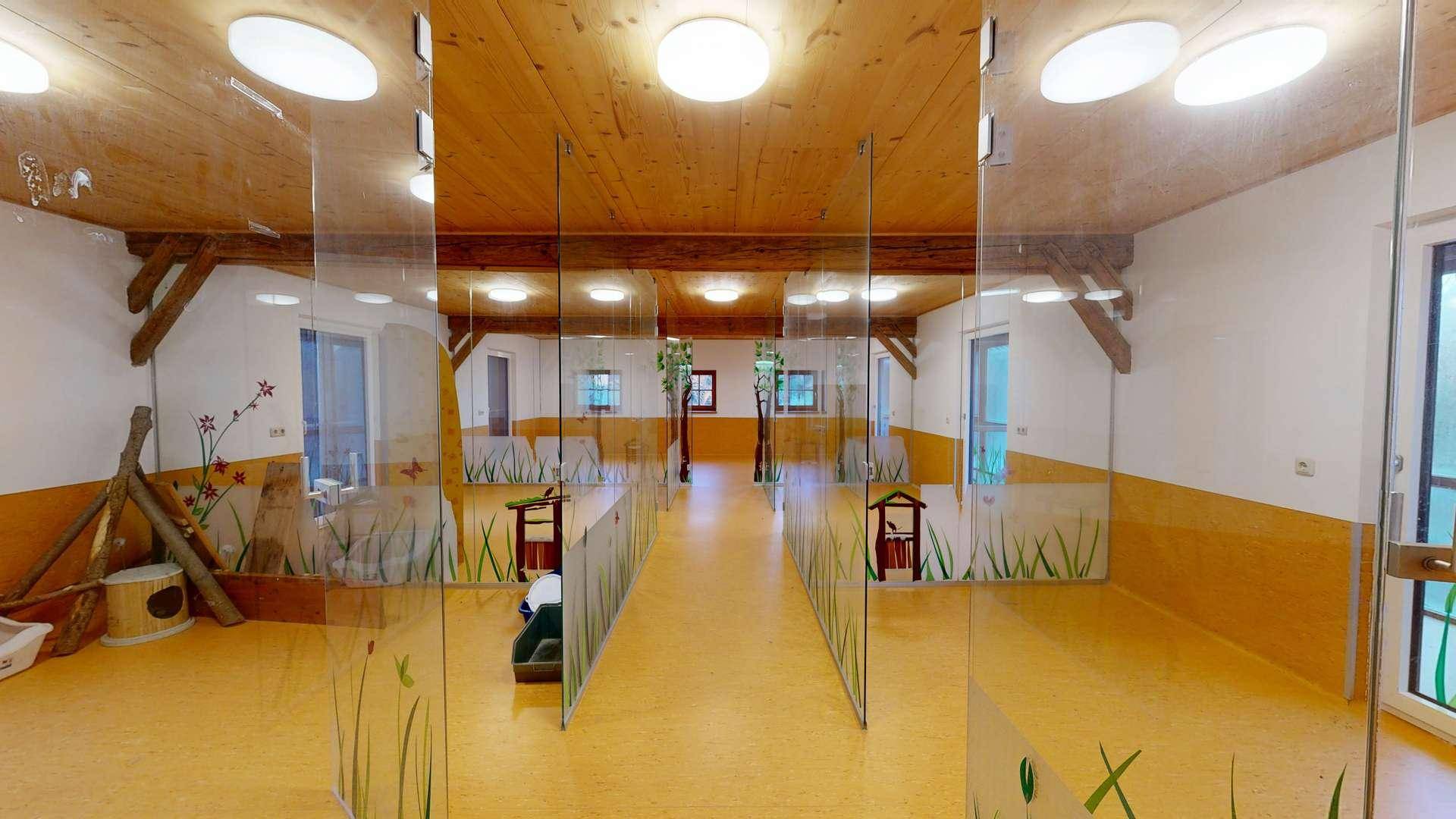 Heller Innenraum mit Holzbalkendecke, Glasabtrennungen und dekorativen Wandmalereien.