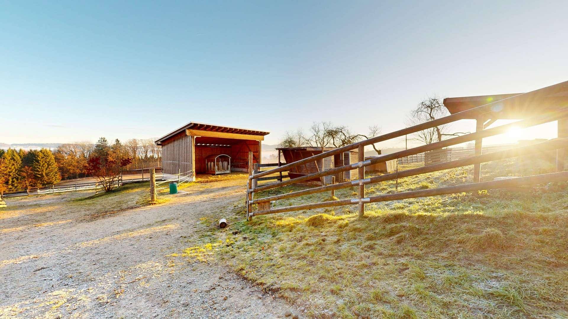 Ländliche Szene mit Holzschuppen, Zaun und weitem Blick in der Morgensonne.