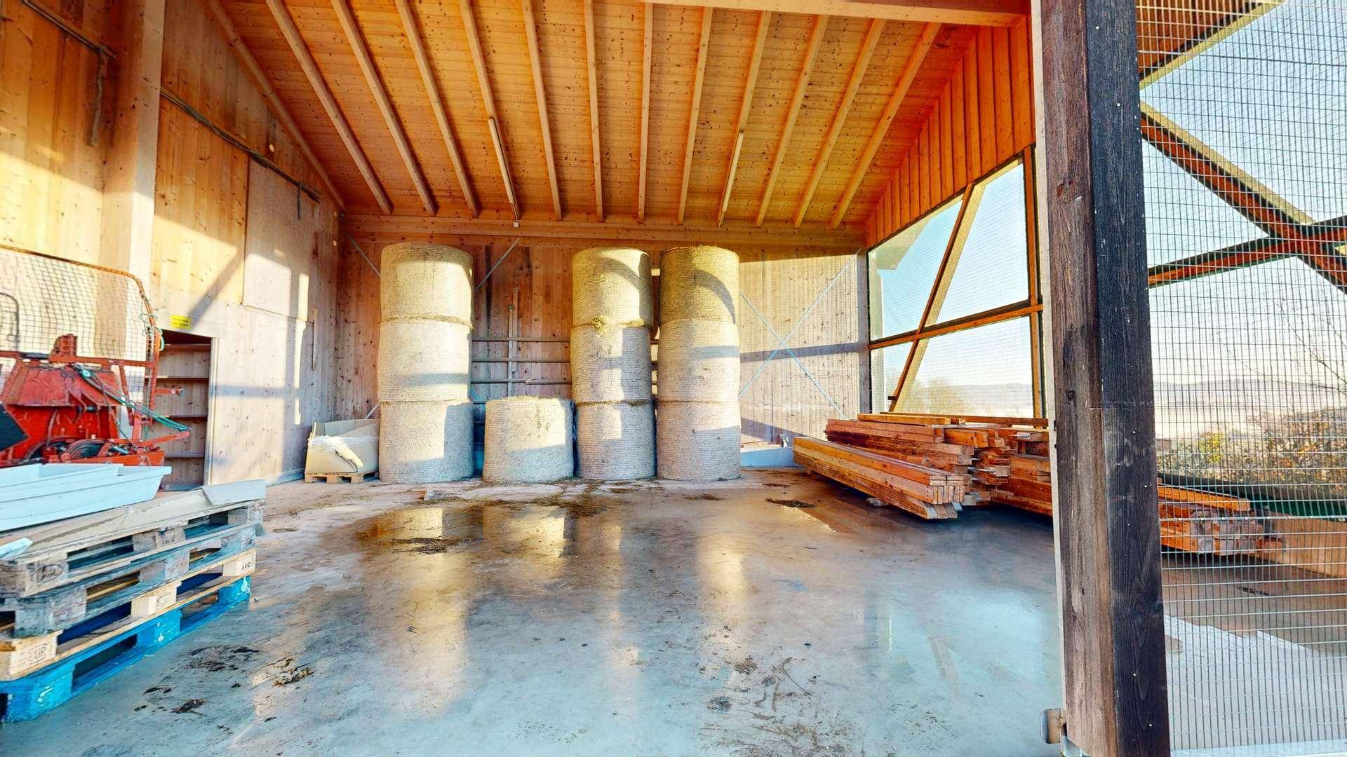 Großer Lagerraum in einer Scheune mit Heuballen und Holzstapeln.