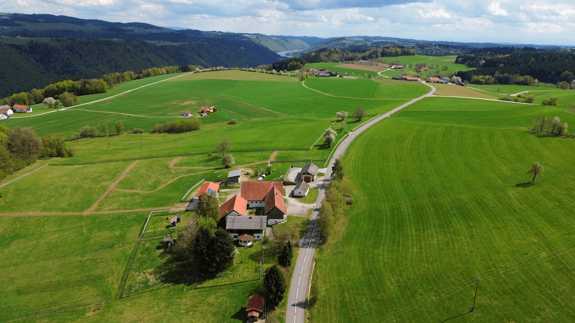 Weitläufige Luftaufnahme einer ländlichen Landschaft mit Bauernhof und Fluss im Hintergrund.
