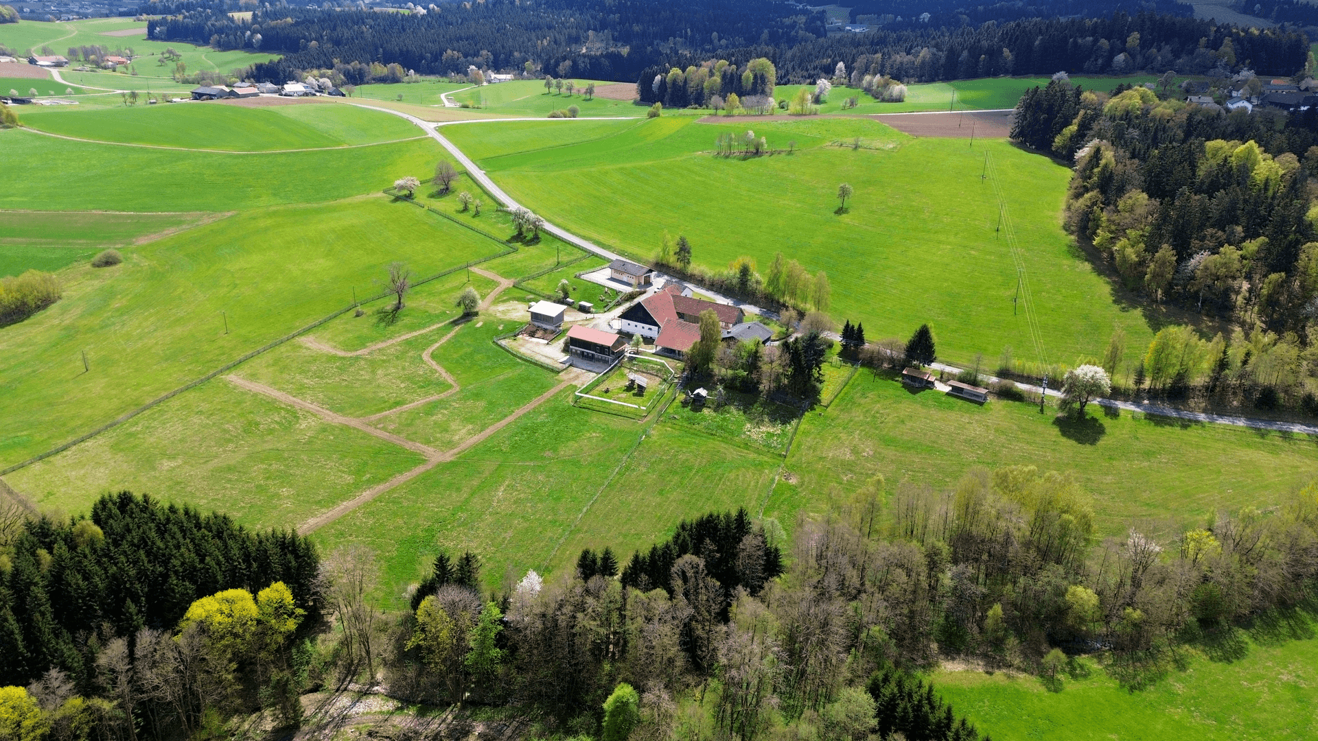 Panoramablick aus der Luft auf ein weitläufiges grünes Gelände mit einem Bauernhof und Wäldern.