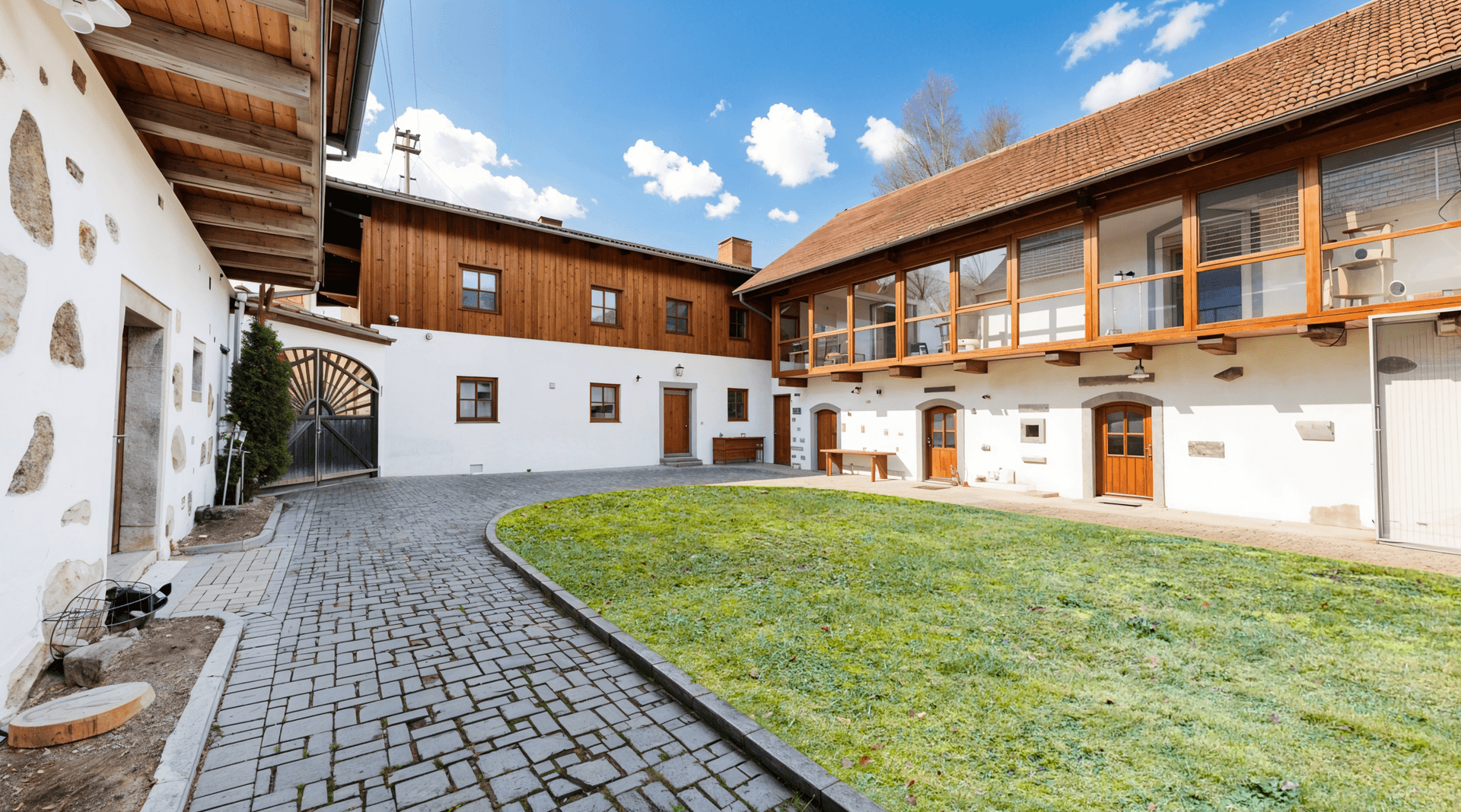 Innenhof eines ländlichen Anwesens mit gepflastertem Weg, Rasenfläche und großen Fenstern.