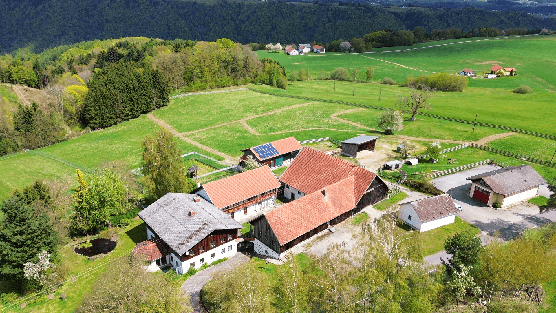 Luftaufnahme eines weitläufigen Anwesens mit mehreren Gebäuden und grüner Umgebung.