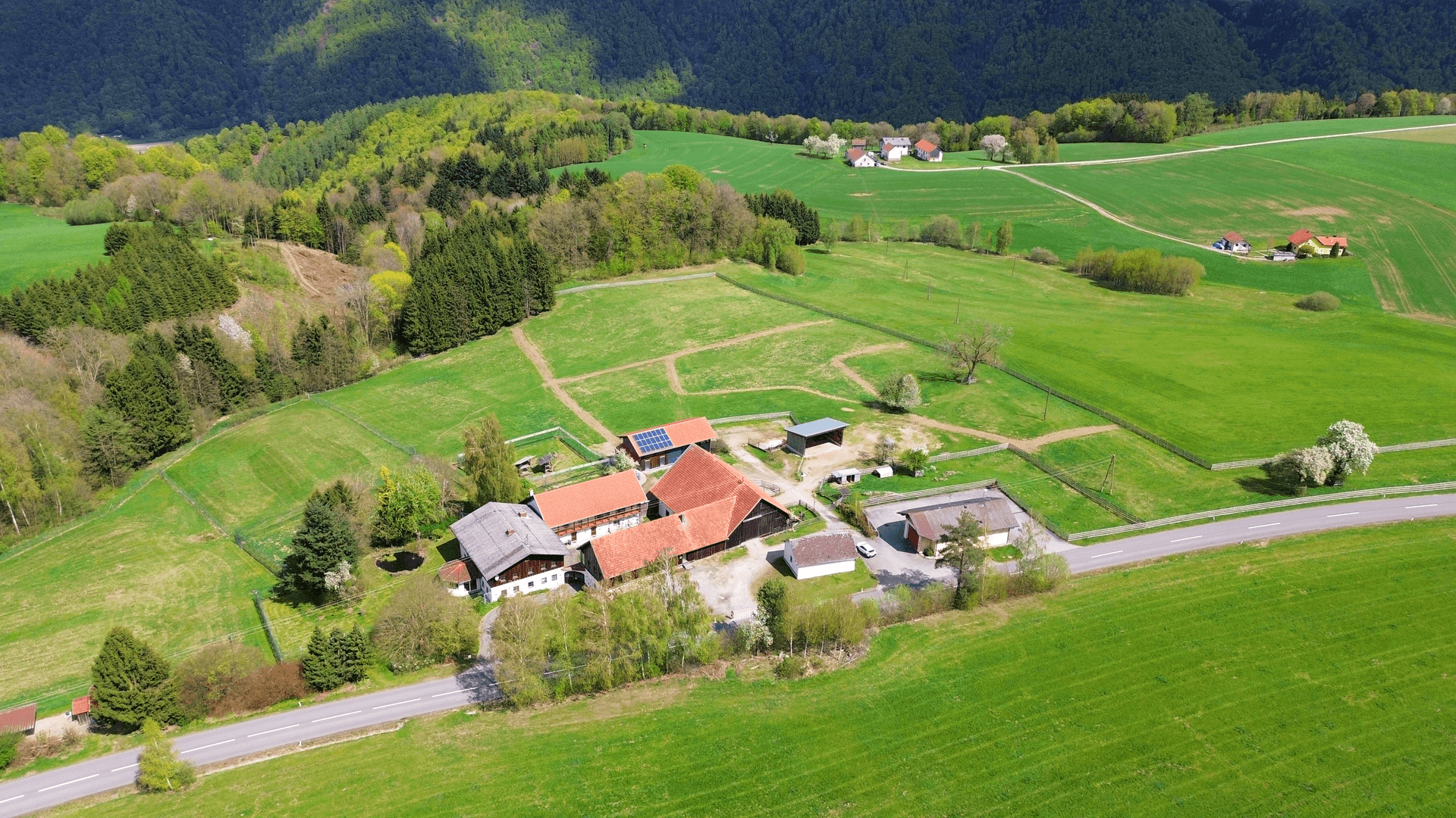 Weitläufige Luftaufnahme eines ländlichen Anwesens umgeben von grünen Feldern und Wäldern.