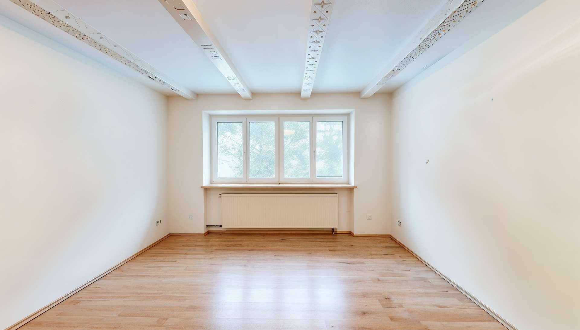 Leerer Raum mit Holzbalkendecke, Parkettboden und großem Fenster für viel Tageslicht.
