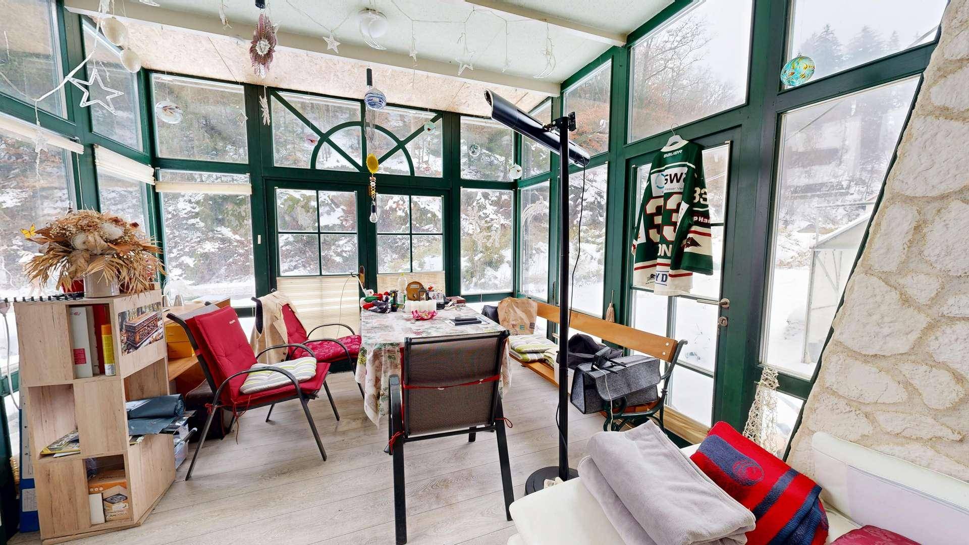 Gemütlicher Wintergarten mit Essbereich, großen Fenstern und Ausblick auf die verschneite Landschaft.