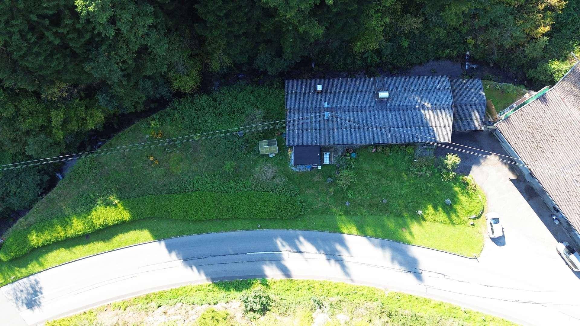 Luftaufnahme des Hauses, umgeben von dichtem Wald und einer Zufahrtsstraße.