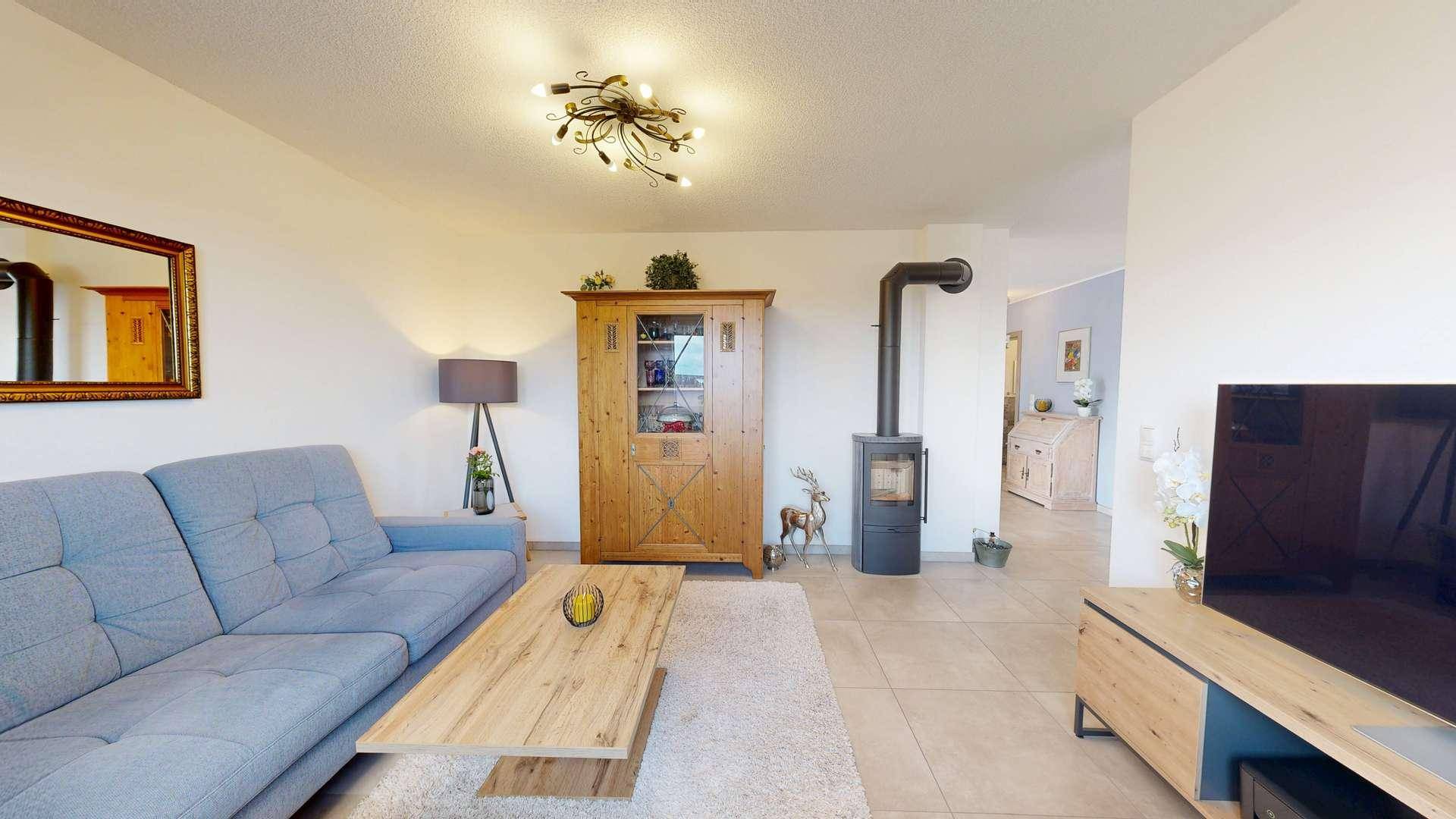 Wohnzimmer mit blauer Couch, Holztisch und traditionellem Schrank, ergänzt durch einen gemütlichen Holzofen.