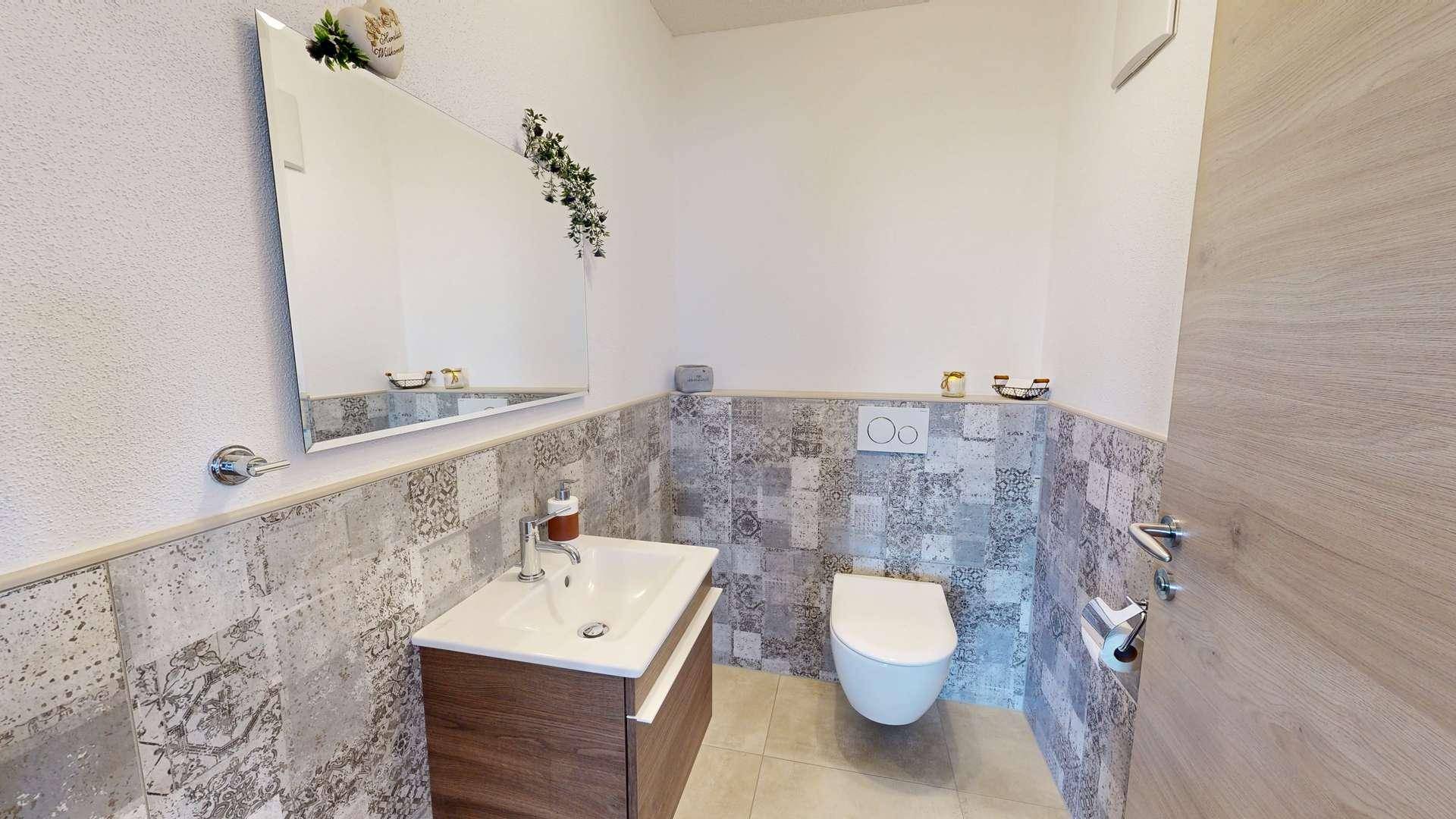 Gäste-WC mit Einzelwaschbecken, Wand-WC und dekorativen Fliesen, praktisch und stilvoll gestaltet.