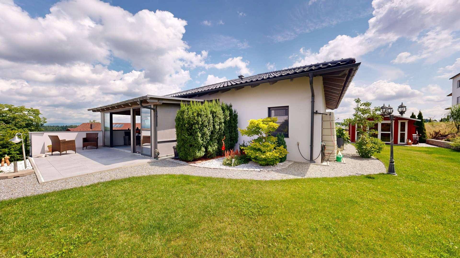 Seitenansicht des Hauses mit gepflegtem Rasen, Gartenbeeten und der angrenzenden Sonnenterrasse.