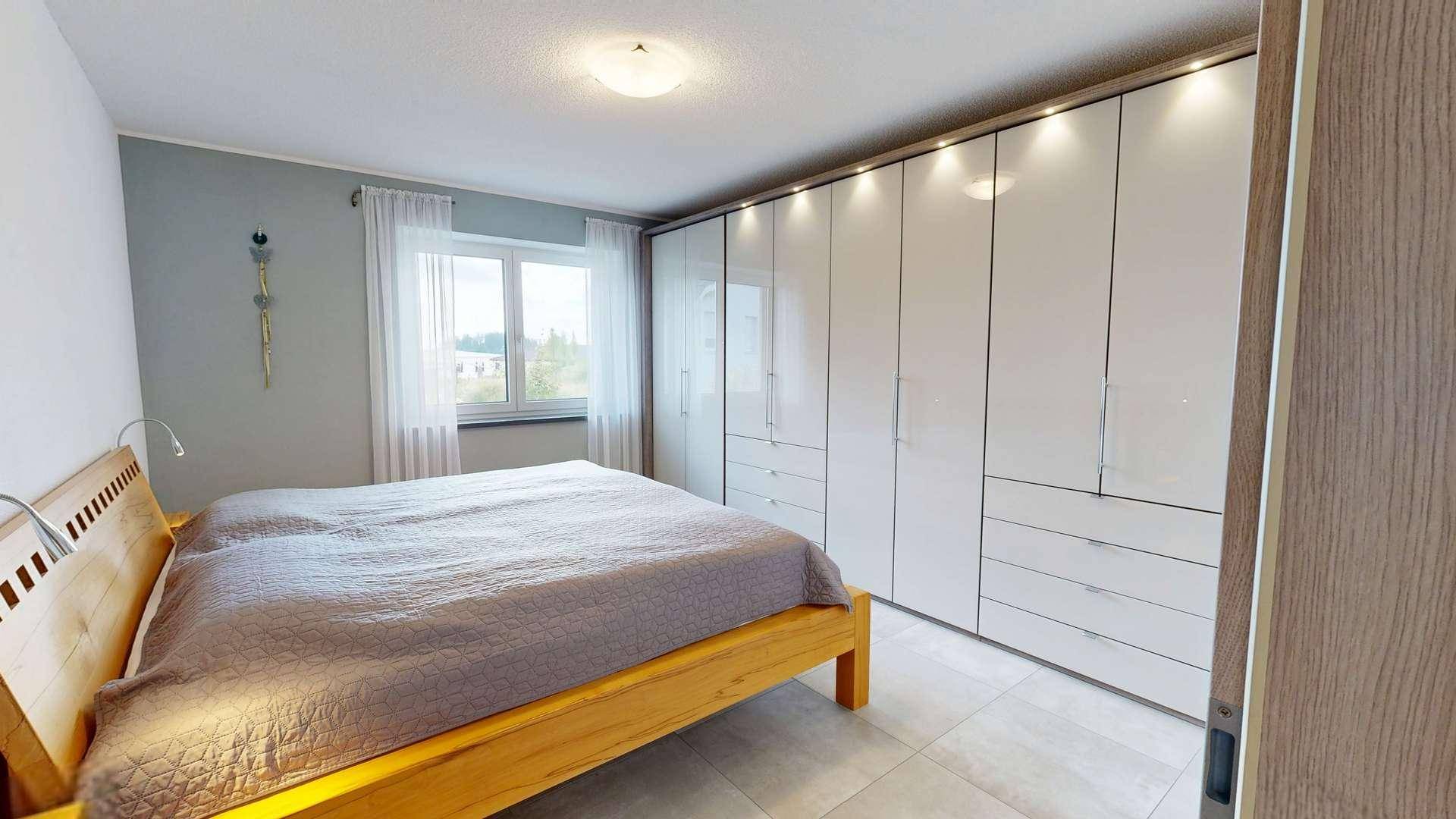 Schlafzimmer mit Holzbett und großem weißen Einbauschrank, graue Wände und Fliesenboden.