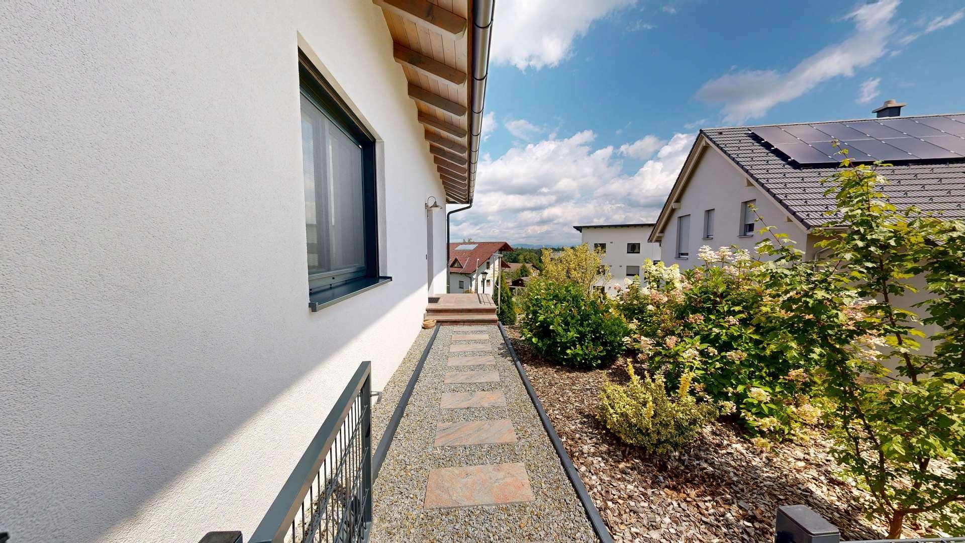 Seitenansicht eines modernen Hauses mit einem gepflasterten Weg und grüner Bepflanzung.