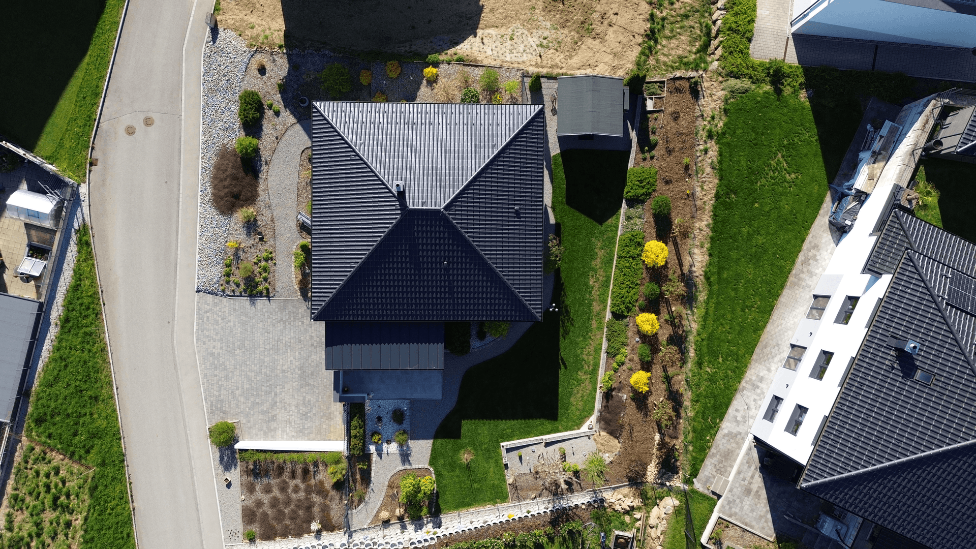 Draufsicht des Hauses mit Satteldach, Gartenanlage und gepflasterter Auffahrt, umgeben von Grünflächen.
