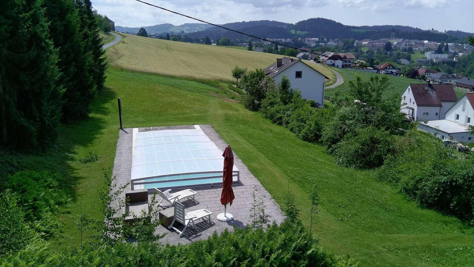 Blick von oben auf den Außenpoolbereich mit Liegestühlen und weitem Blick ins Grüne.