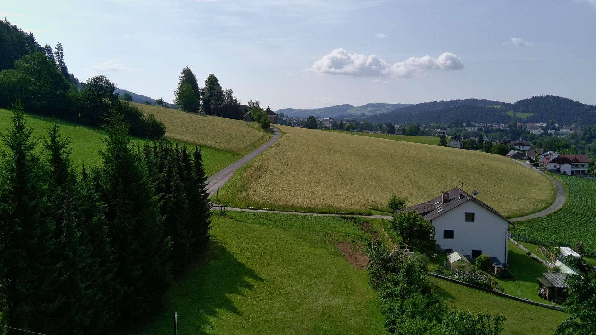 Weitläufige Aussicht auf sanfte grüne Hügel, Felder und ein charmantes Haus in ländlicher Umgebung.