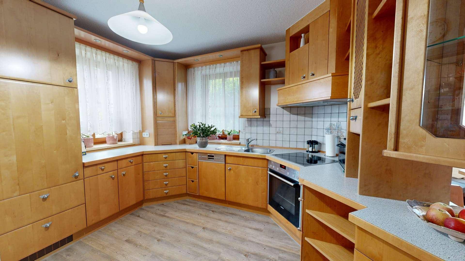 Funktionale Küche mit hellen Holzschränken, Einbaugeräten und Fliesenrückwand.