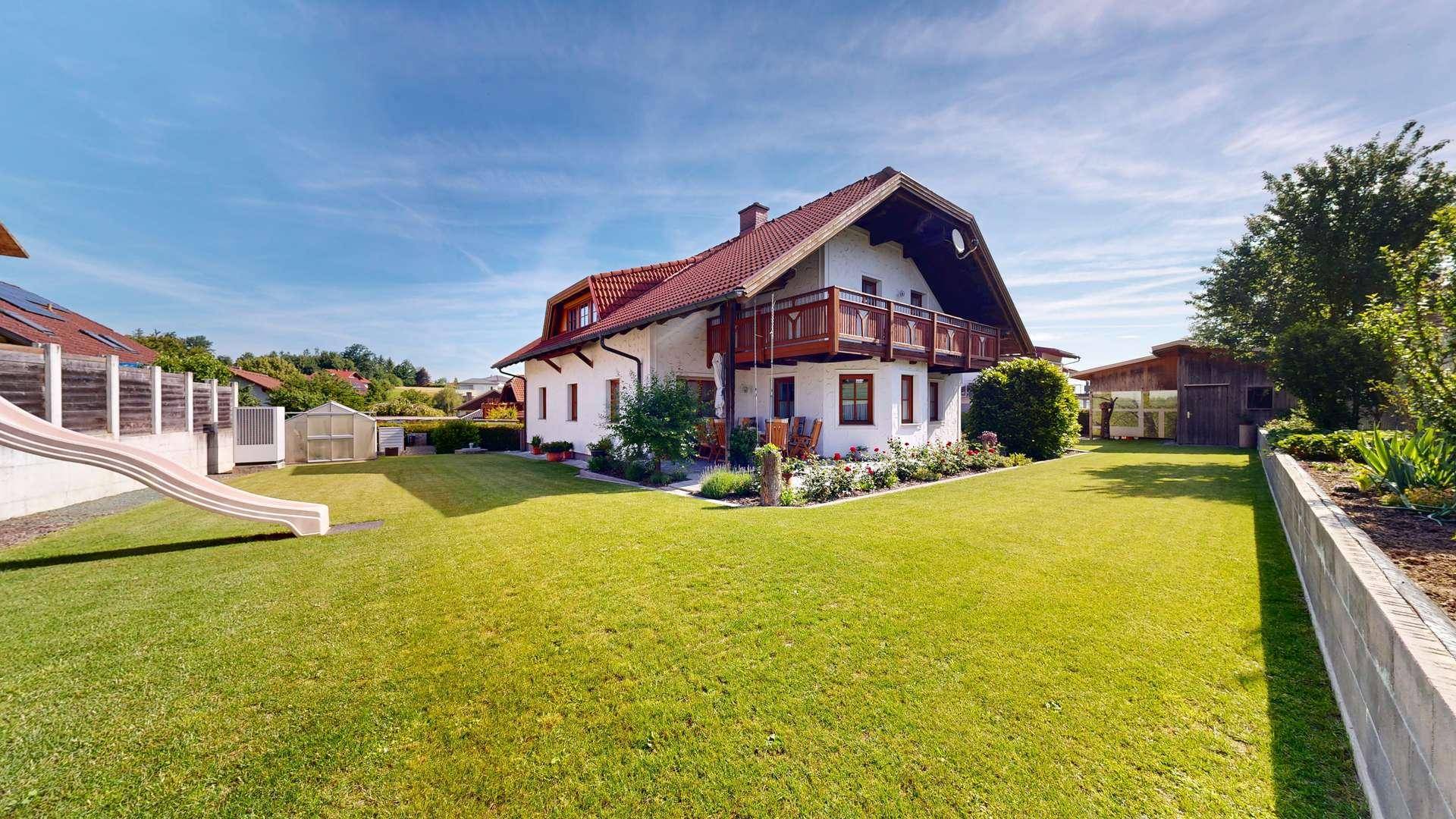 Gepflegter Garten mit Rasenfläche, Kinderrutsche und Blick auf das Haus.