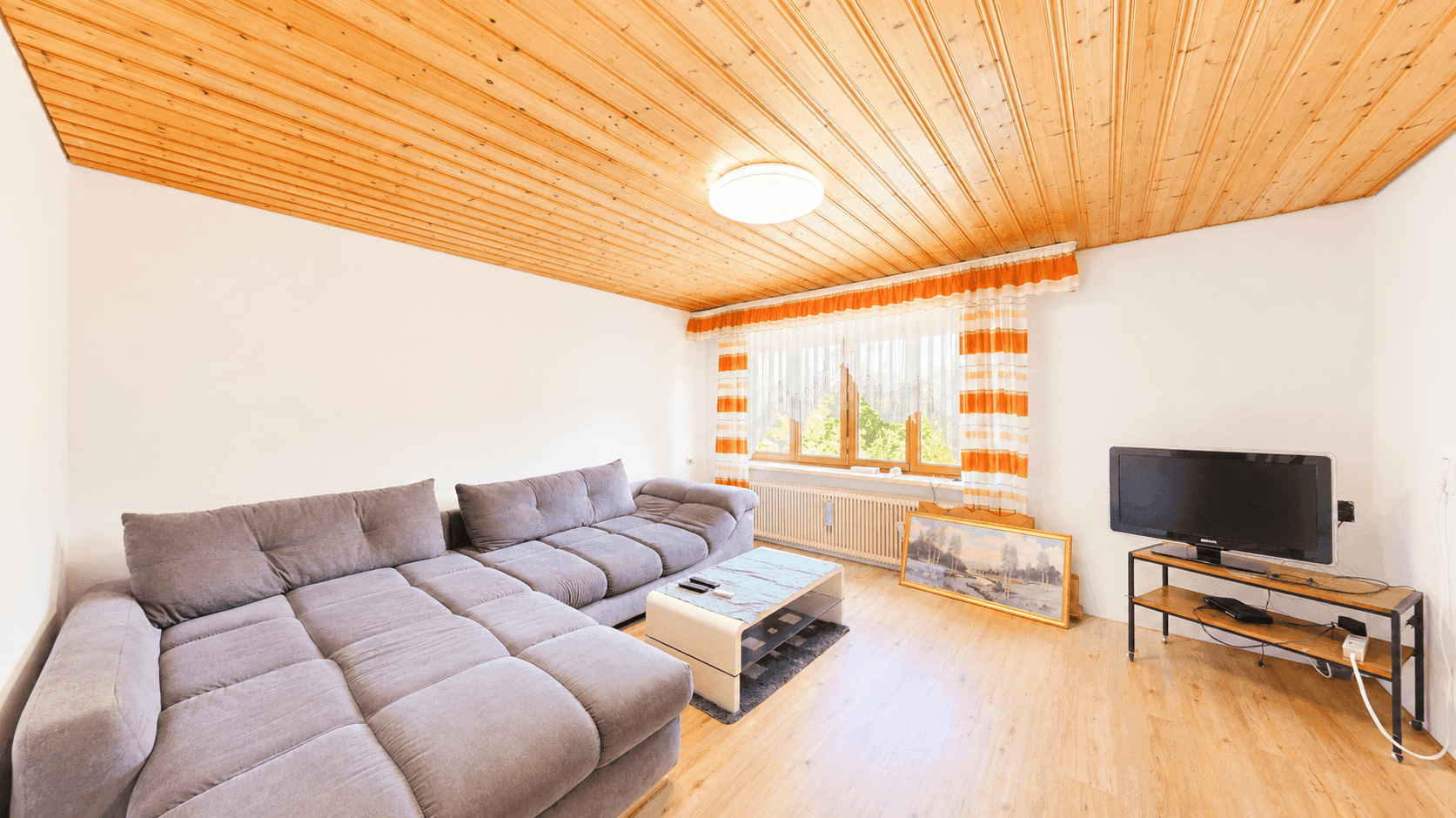 Geräumiges Wohnzimmer mit großem Ecksofa, Laminatboden und einer Holzdeckenverkleidung, hell und einladend.