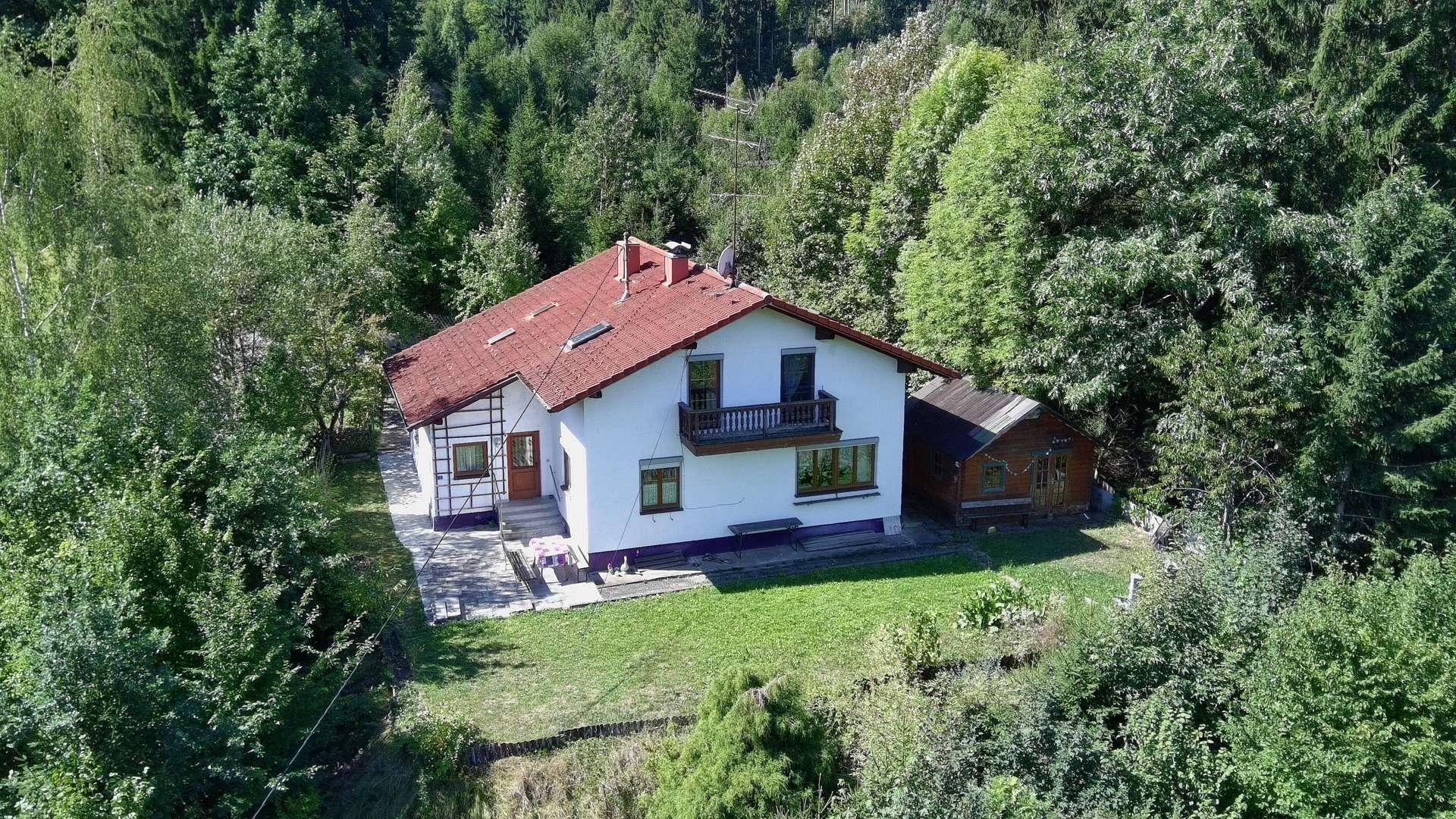 Luftaufnahme eines freistehenden Hauses mit rotem Ziegeldach, eingebettet in eine waldreiche Umgebung.