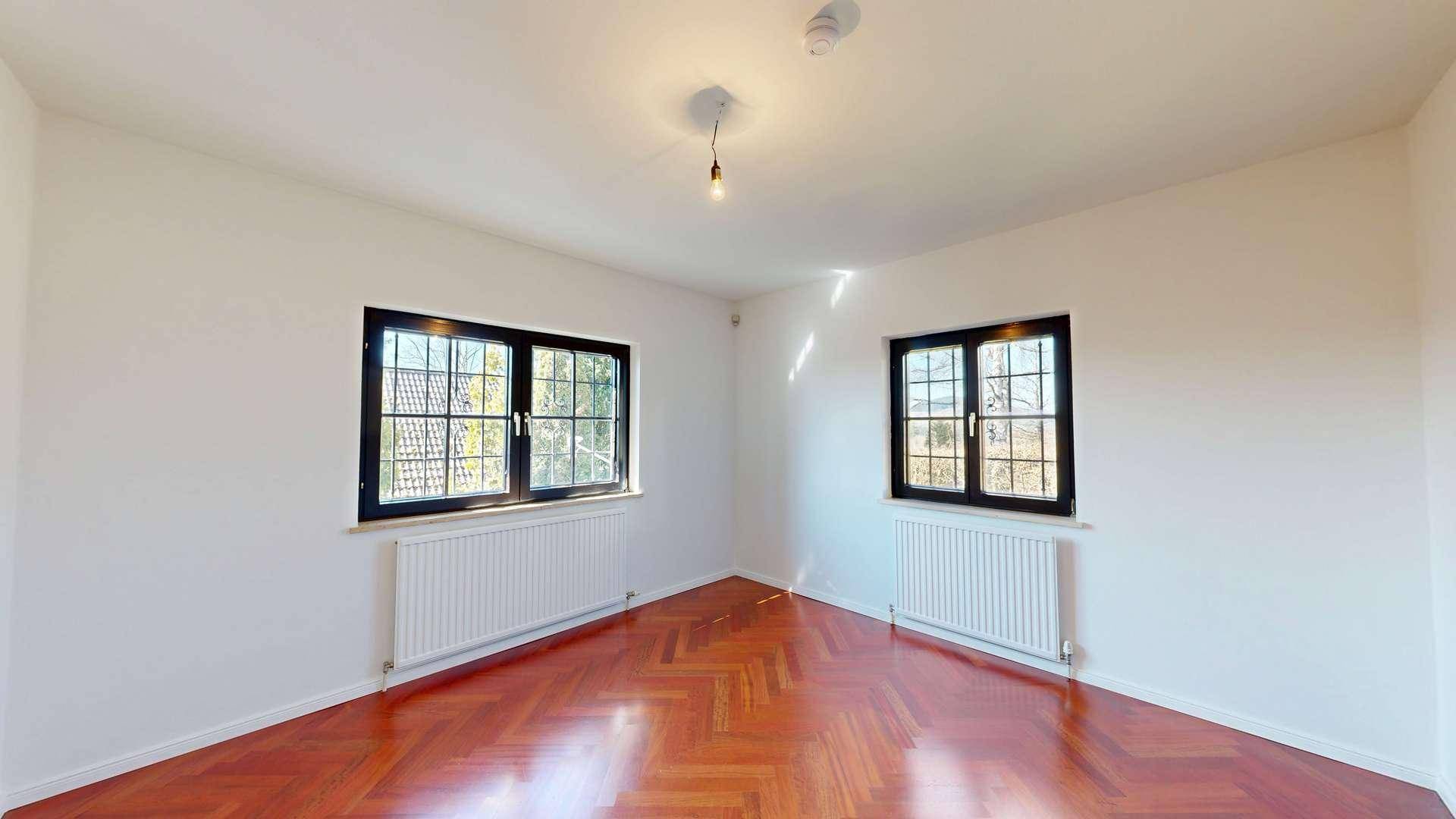 Geräumiges, helles Zimmer mit Fischgrätparkett und zwei Fenstern, ideal als Schlaf- oder Arbeitszimmer.