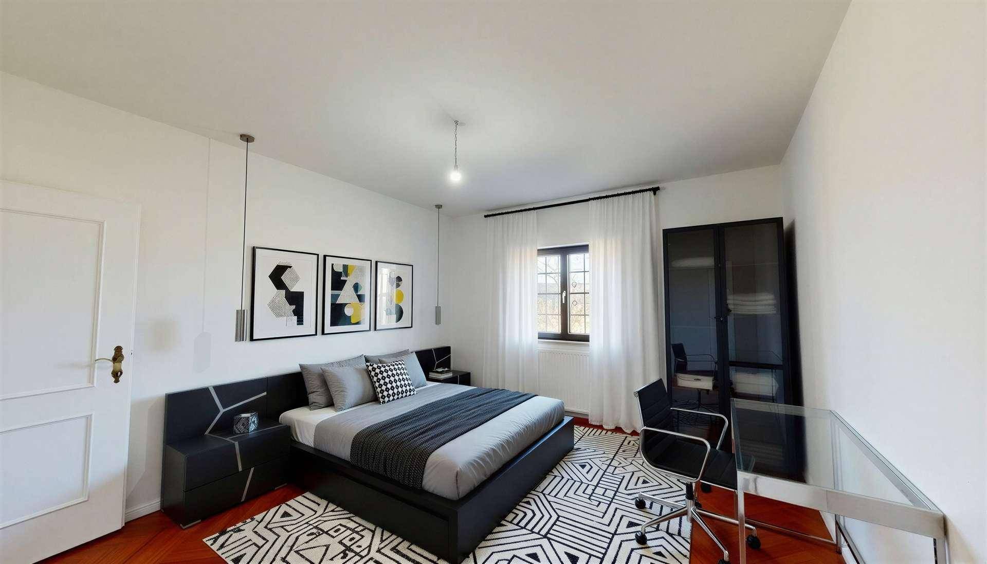Modern eingerichtetes Schlafzimmer mit Fischgrätparkett, großem Bett und Arbeitsbereich am Fenster.