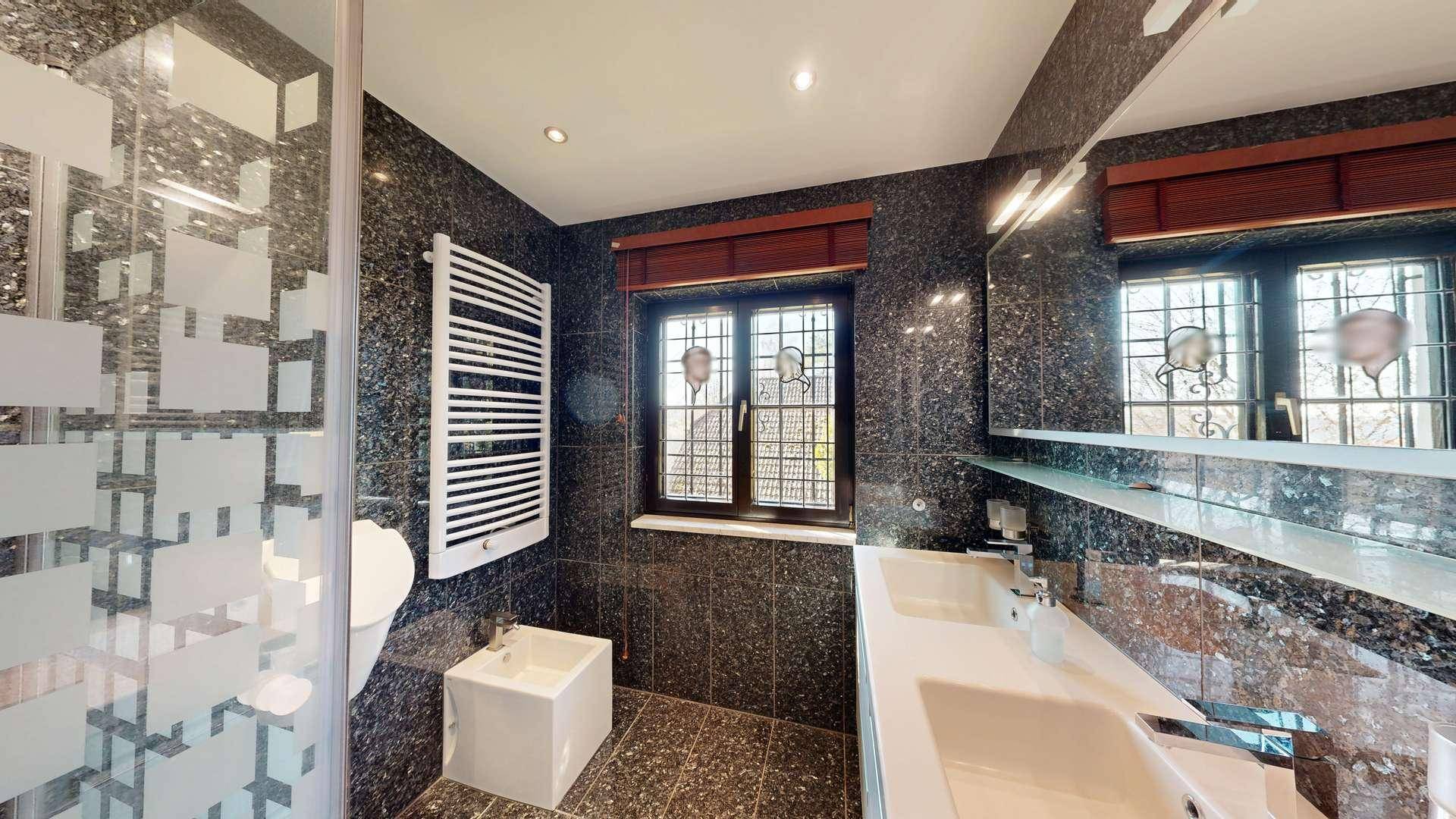 Elegantes Badezimmer mit dunklen Granitfliesen, Doppelwaschbecken, Bidet und Duschbereich.