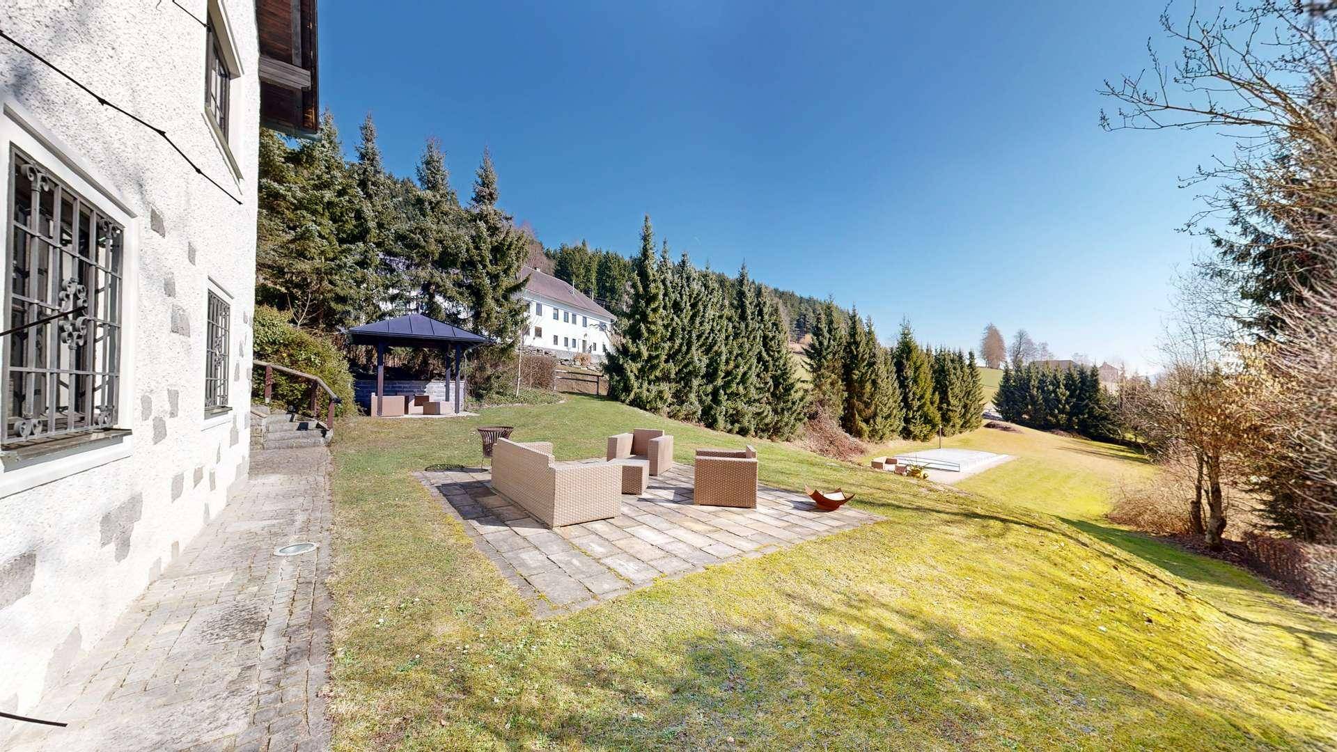 Großer Garten mit gepflasterter Terrasse und bequemen Outdoor-Möbeln, umgeben von viel Grün.