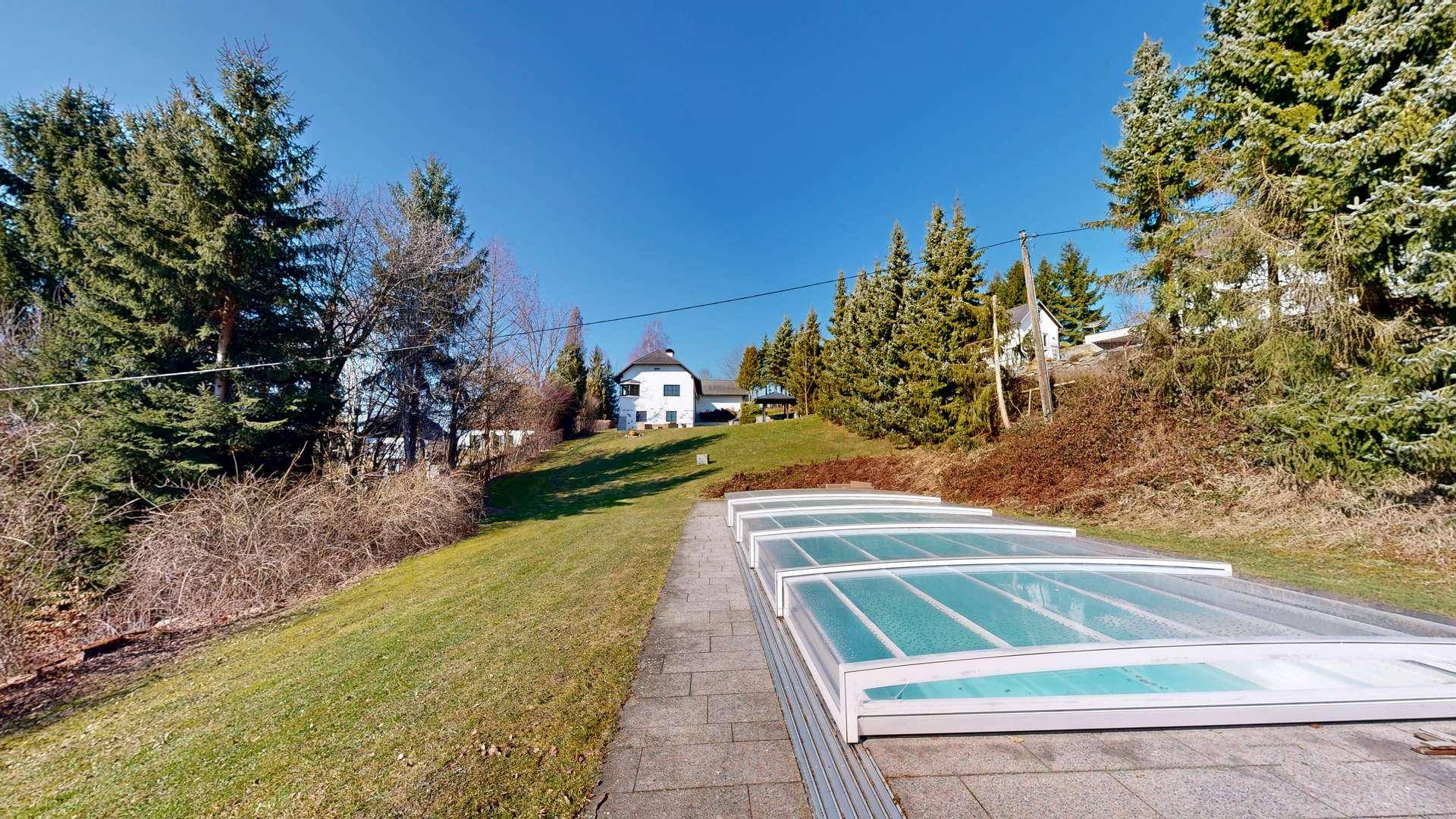 Weitläufiger Außenbereich mit überdachtem Pool und Blick auf das Anwesen in der Ferne.