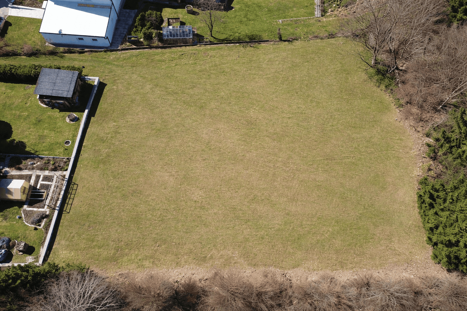 Luftaufnahme eines großen Feldes mit grünen und trockeneren Grasflächen, umgeben von Vegetation und Häusern.