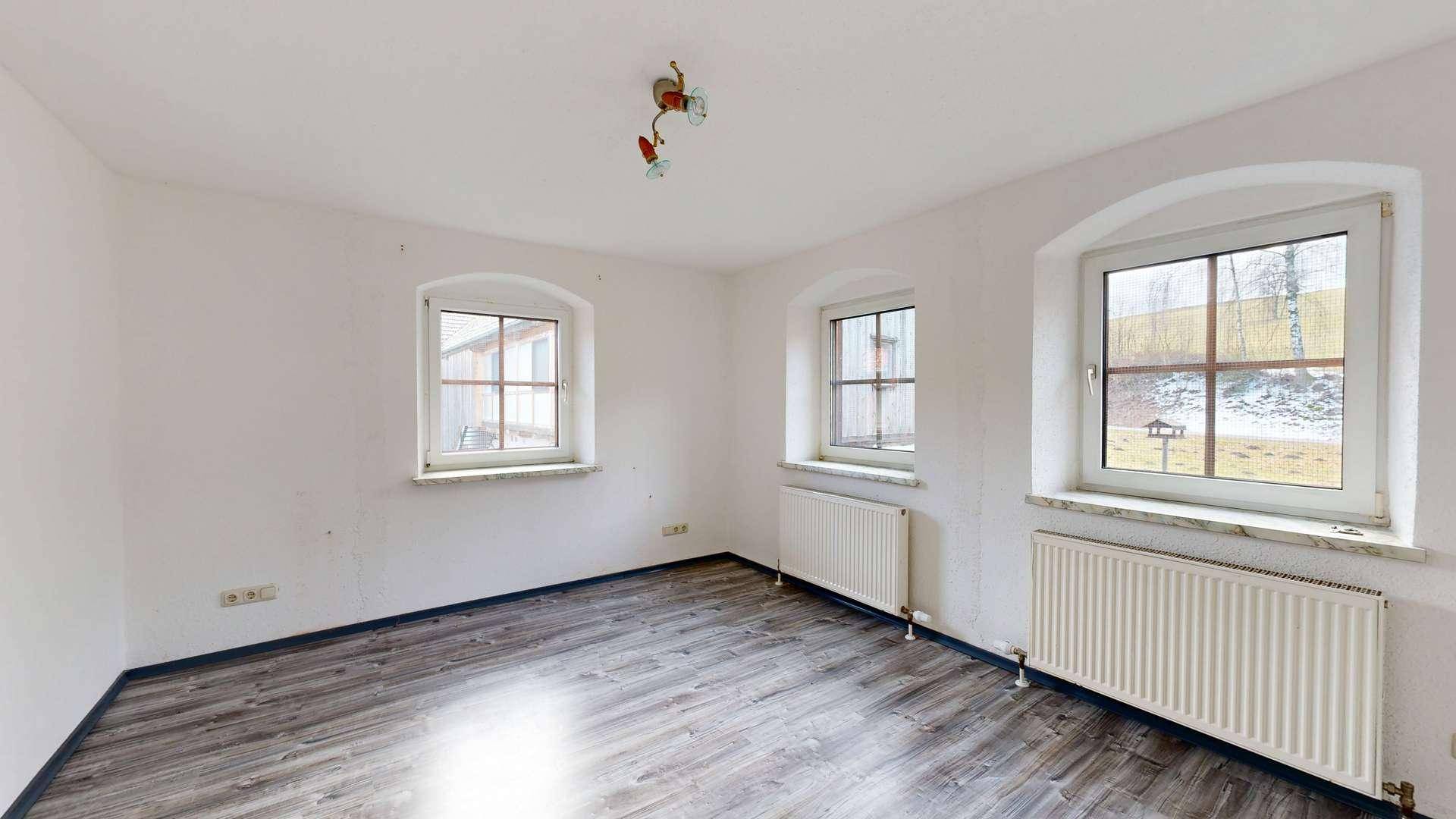 Leerer Raum mit Laminatboden, drei Fenstern und Heizkörpern.