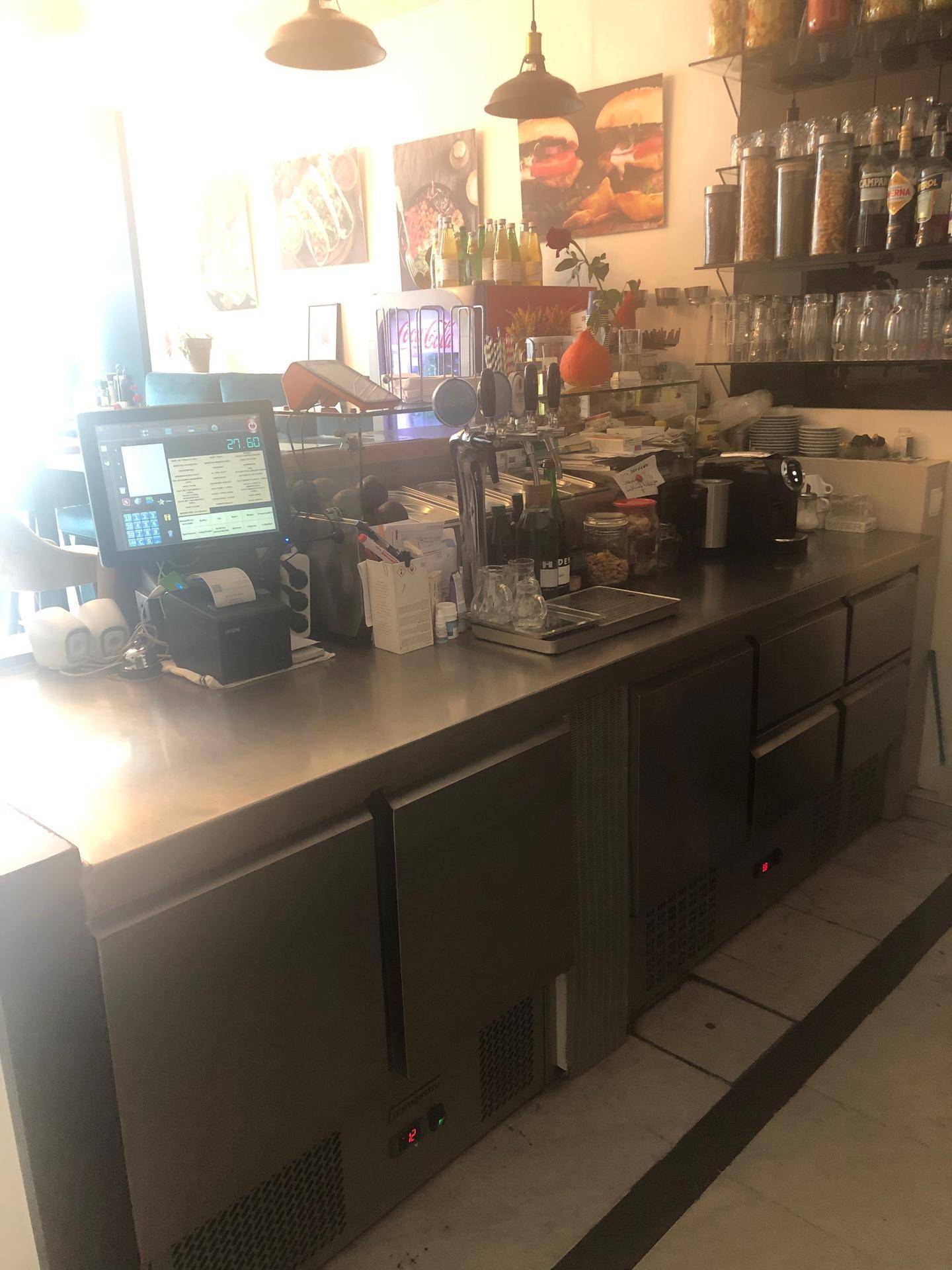 Eine Theke in einer Gewerbeküche mit Kasse, Kaffeemaschine, Zapfanlage und Regalen mit Vorräten.