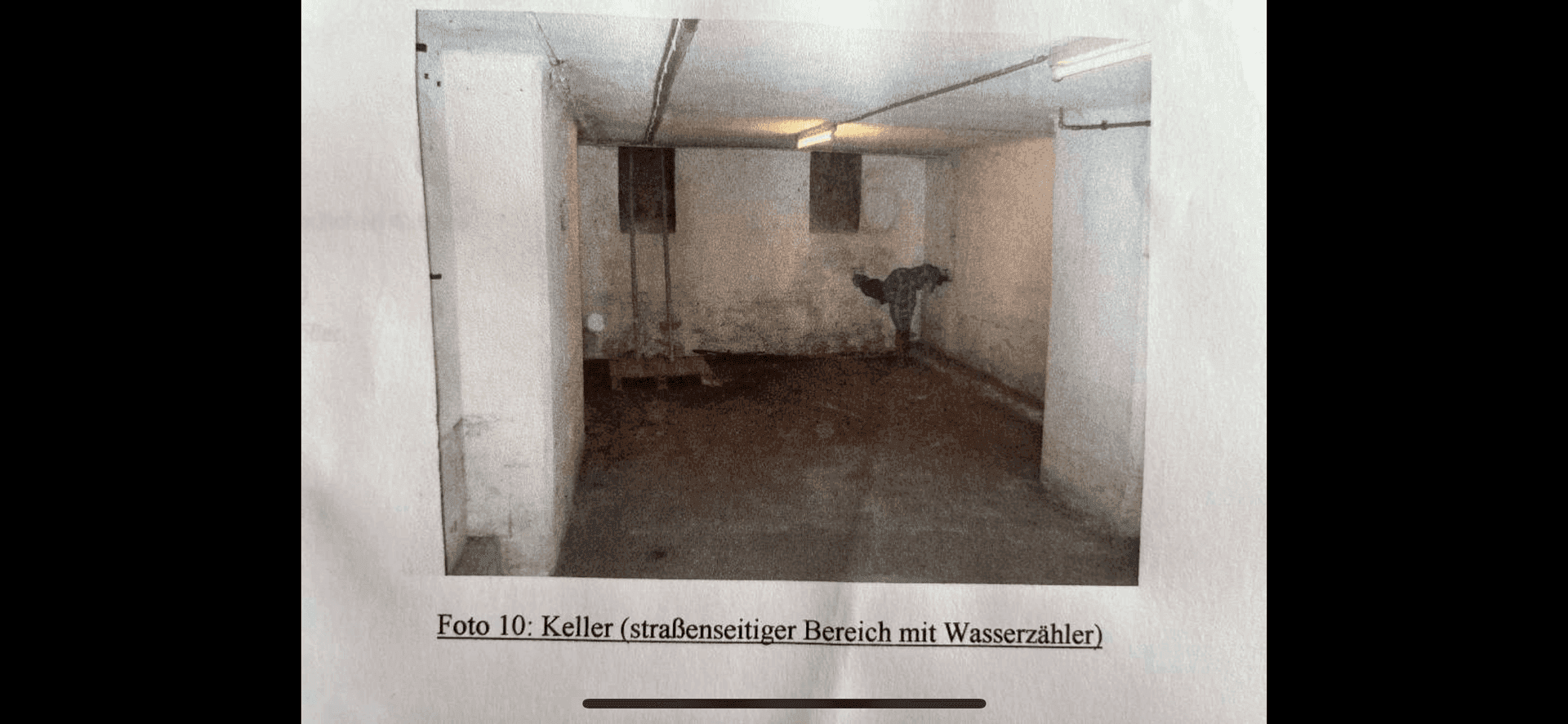 Foto eines Kellerraums mit Wasserzähler, rauen Wänden und dunklem Boden in einem älteren Gebäude.